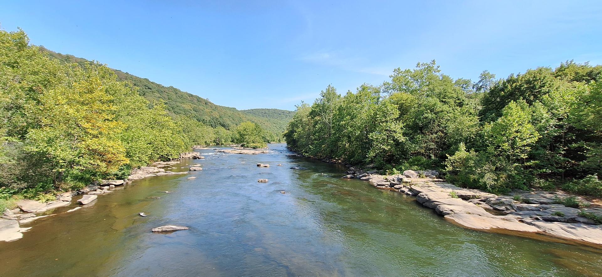 Wide river flowing between lush green forested hills on a clear day.