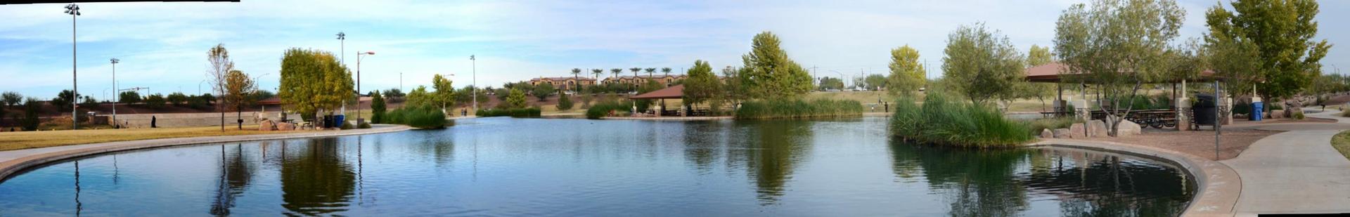 Panoramic view of a calm lake surrounded by trees and a paved path.