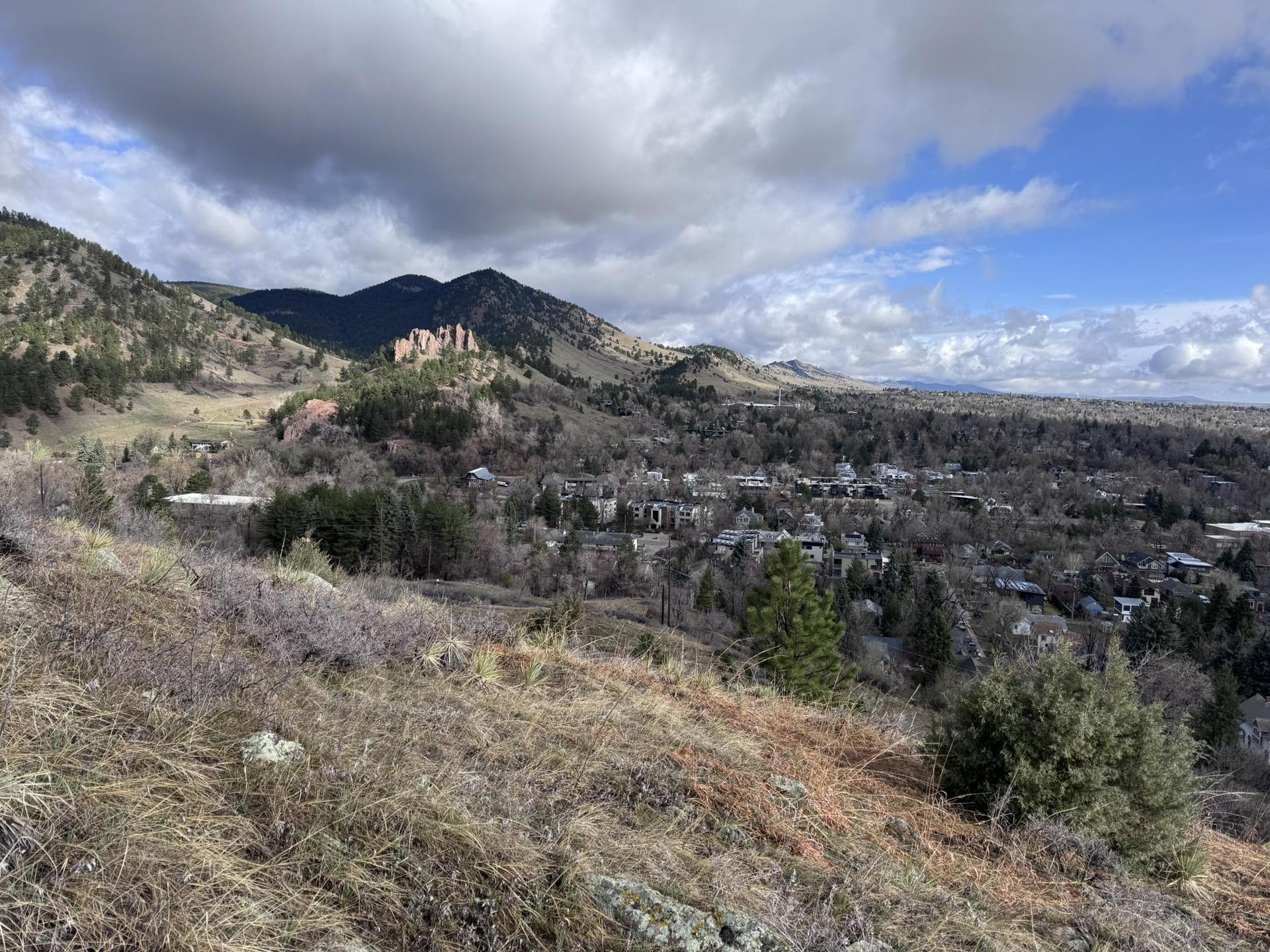 Overlook of a town and mountains from a dry, grassy hill under cloudy skies.