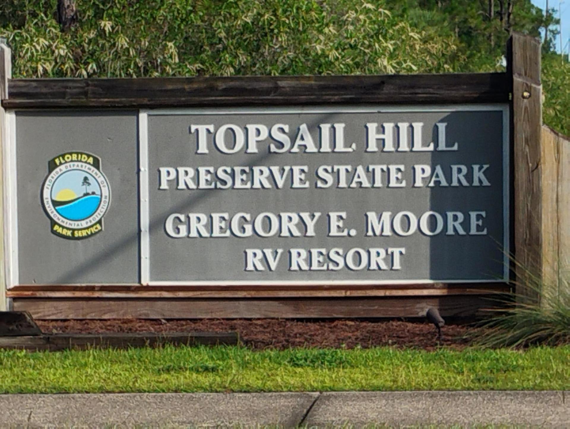 A wooden sign with text and a park service logo, surrounded by grass.