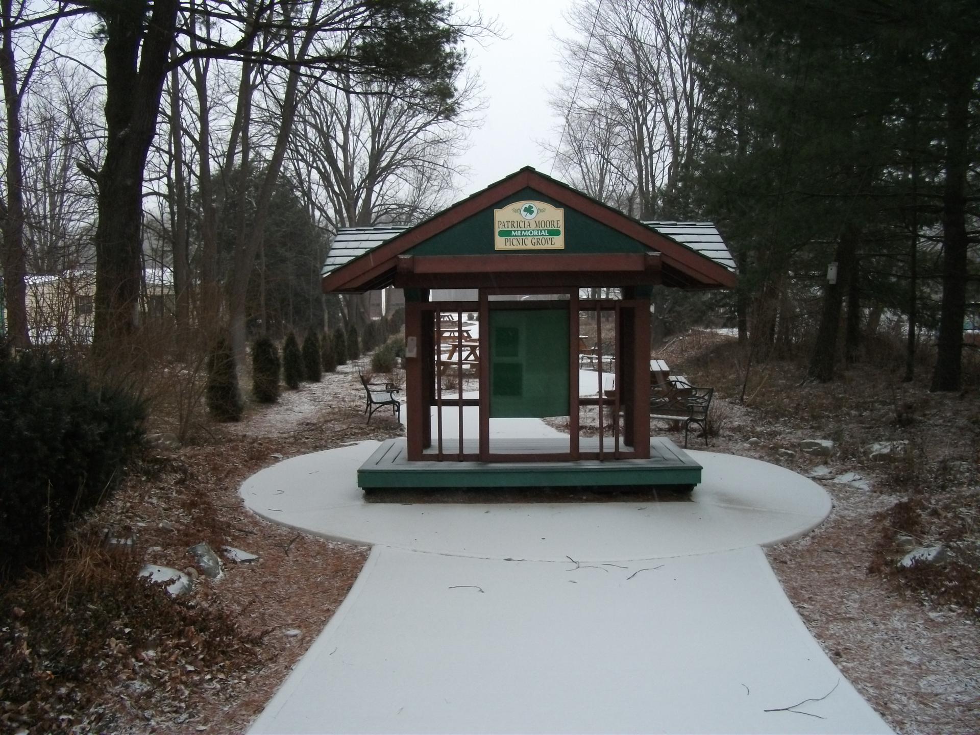 Green and brown shelter on a snow-dusted path, bare trees, overcast day.
