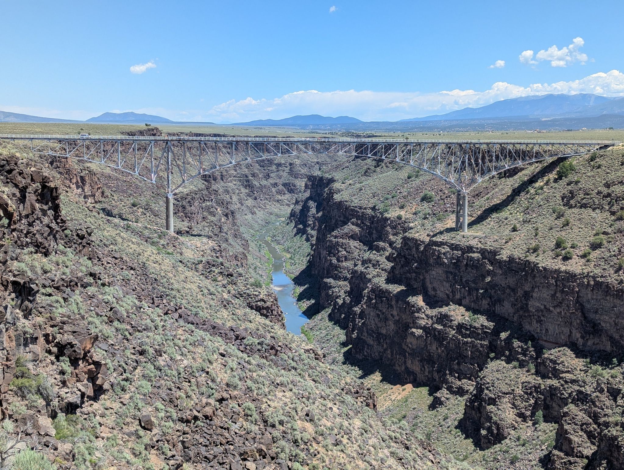 A massive steel bridge crosses a deep, rocky canyon with a river below. - West Rim Trail