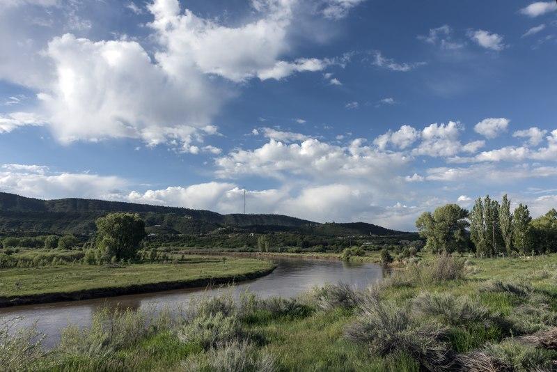 A winding river flows through green banks under a bright, cloudy sky.