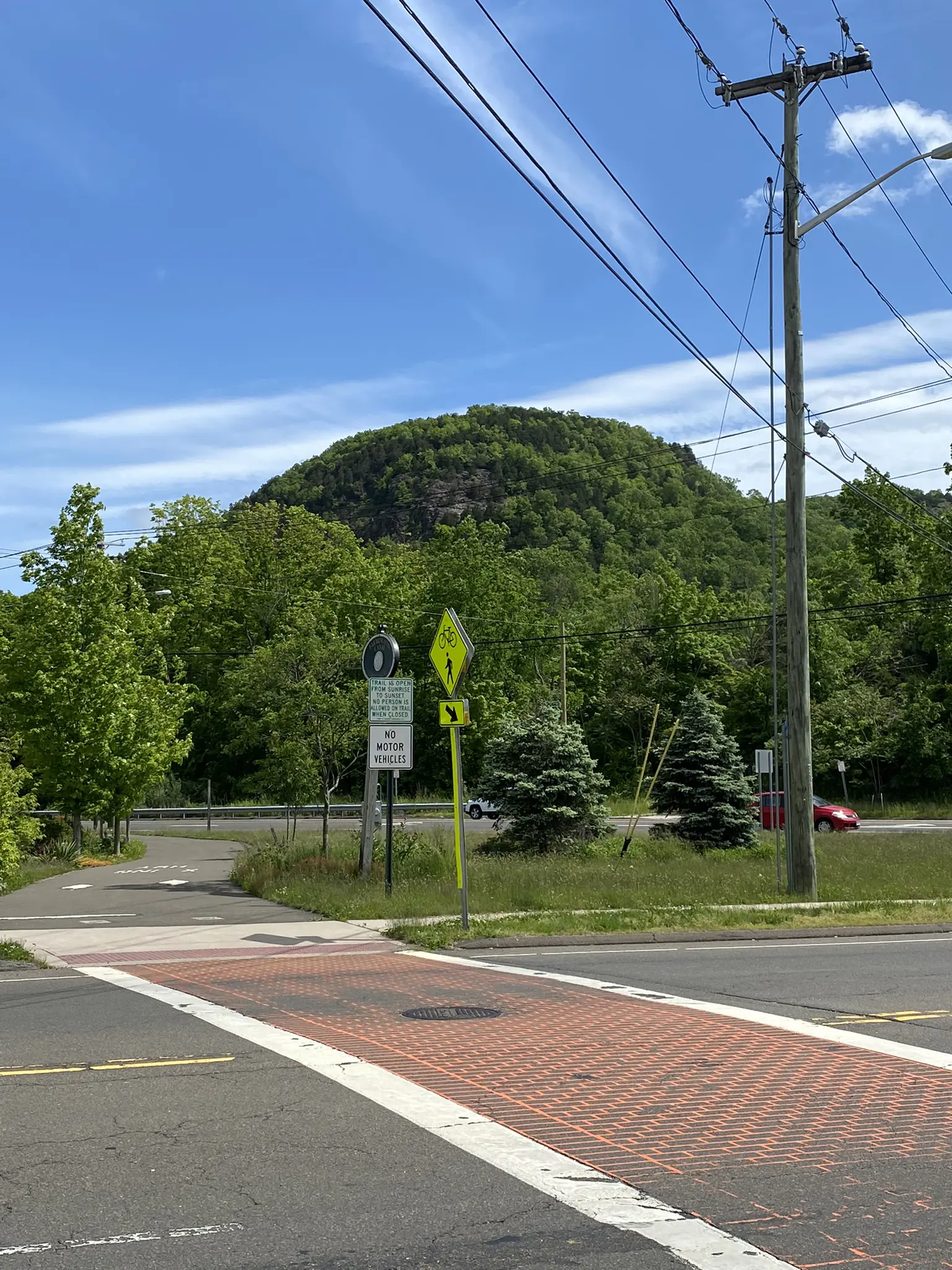 Green forested hill overlooking a street intersection with signs and power lines.
