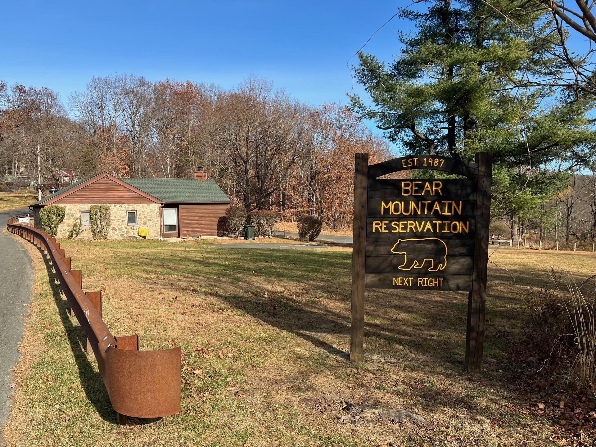 Wooden sign and small building on a sunny day with bare trees.