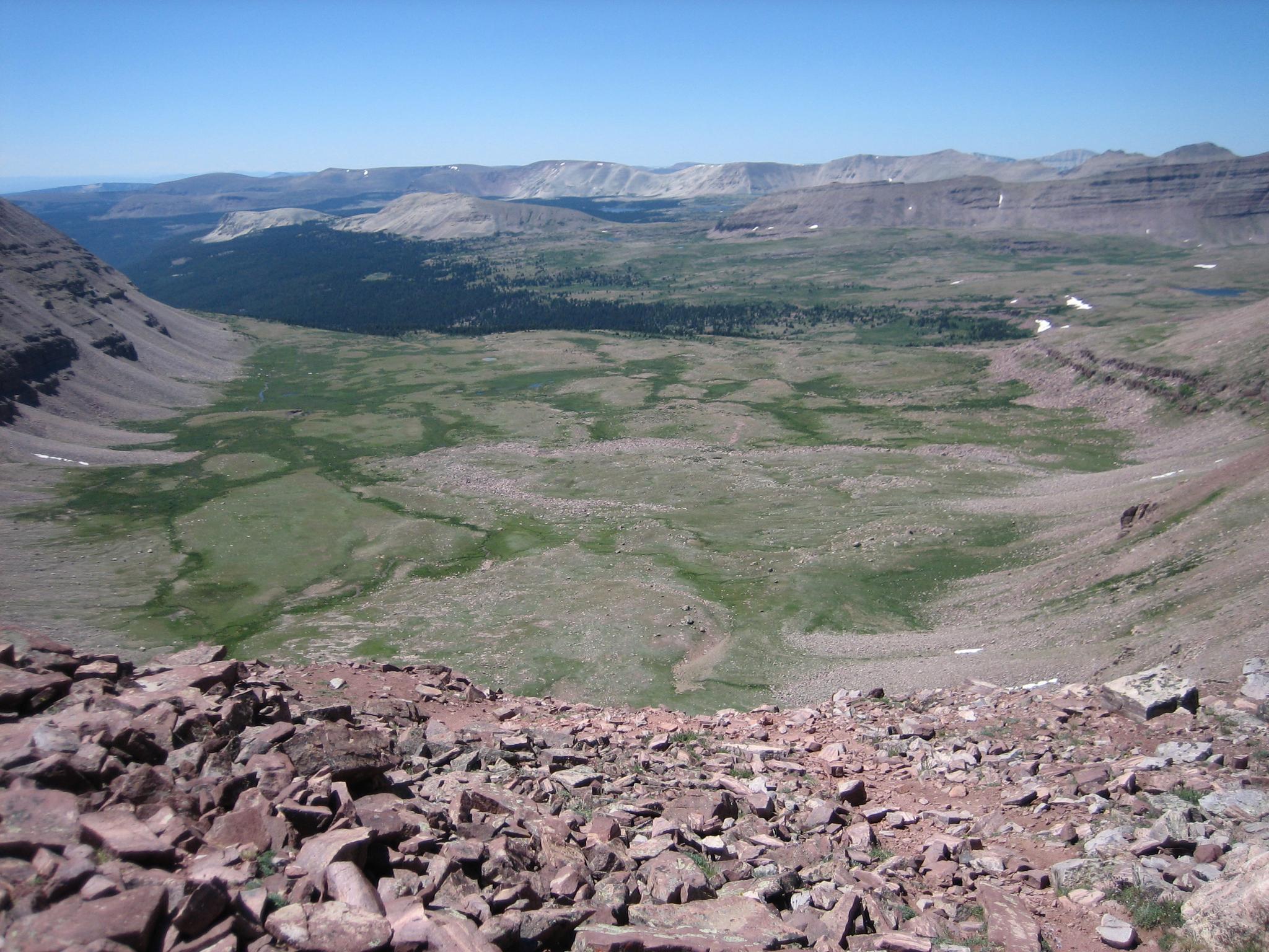 Rocky mountain overlook revealing a vast green valley and distant peaks.