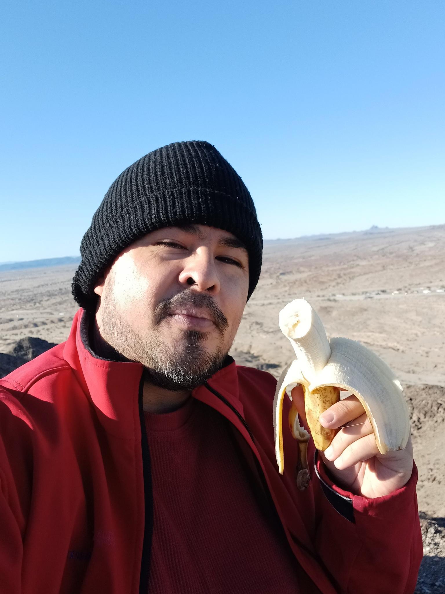 Man holding a peeled banana in a bright, arid outdoor setting.