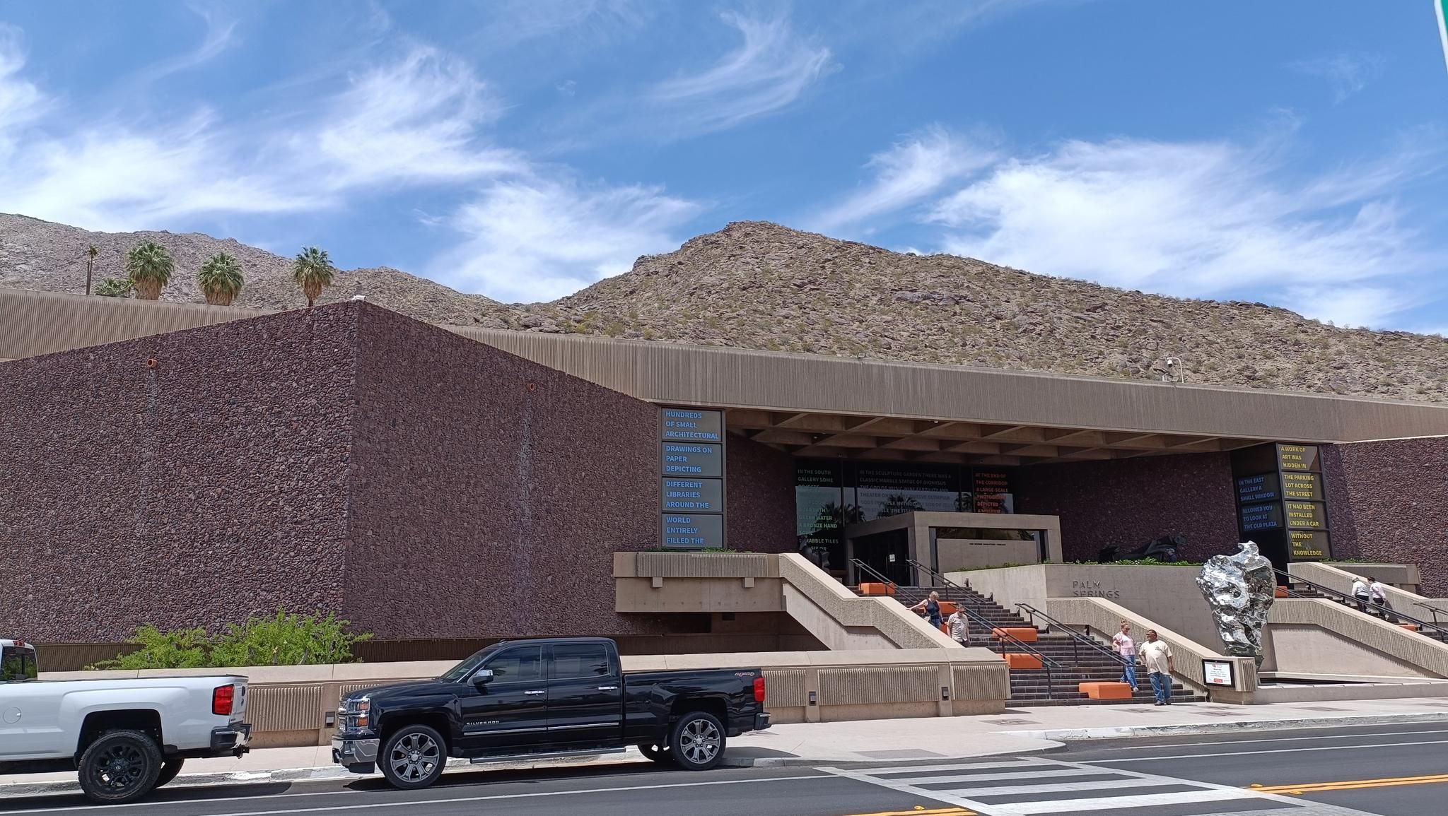 Modern building with textured walls, rocky mountains, and people on steps. - South Palm Canyon Drive to South Sunrise loop