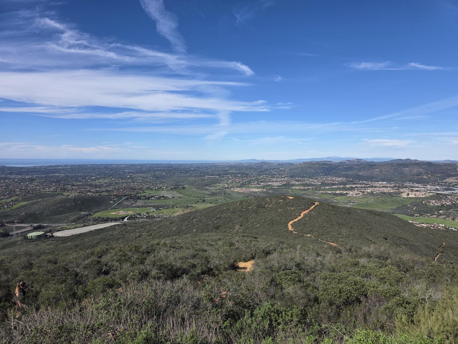 Panoramic view of green hills, distant city, and ocean under a clear sky.
