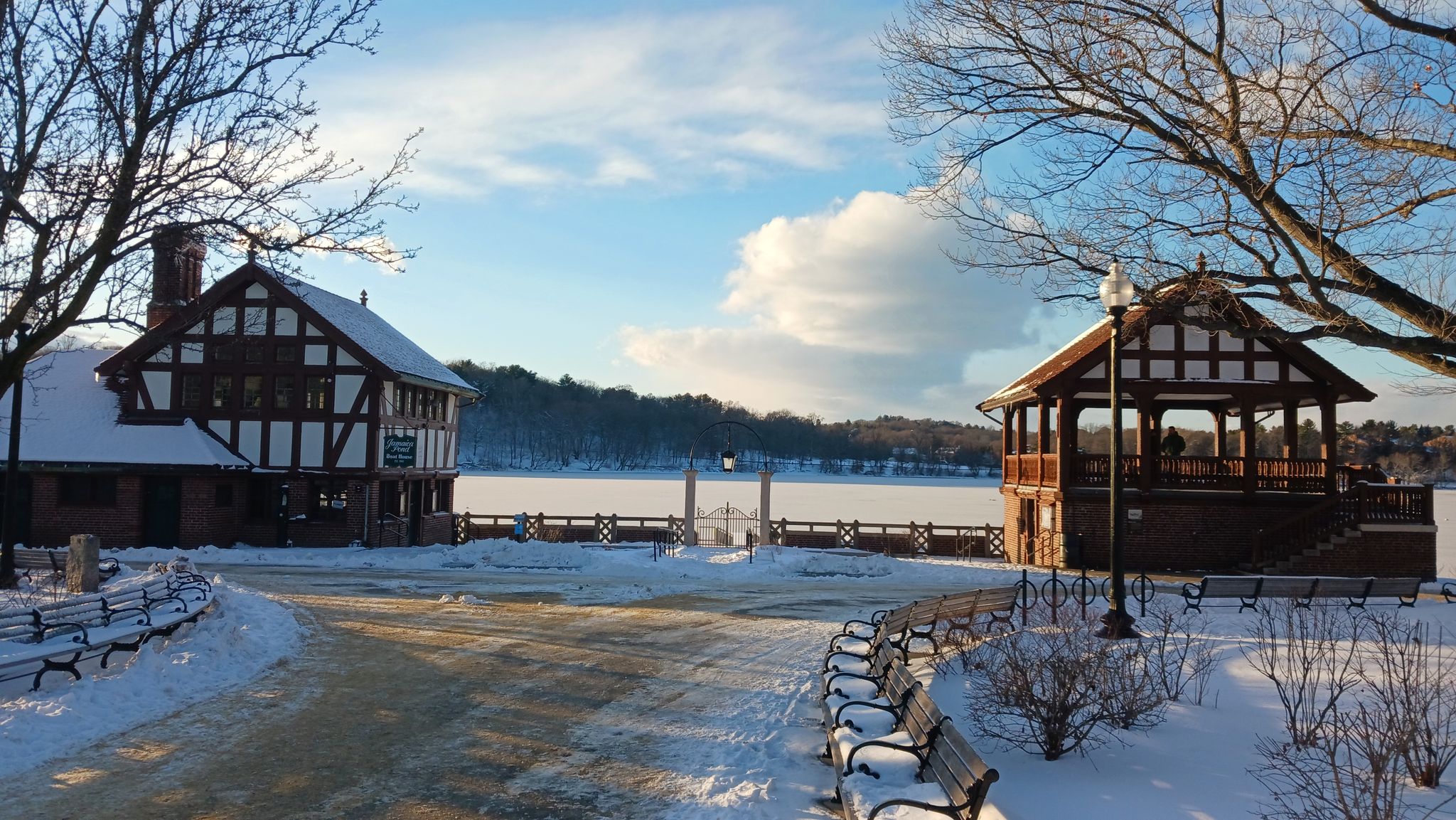 Snow covers the ground around two buildings by a frozen lake. - Southwest Corridor Park & Olmsted Park loop