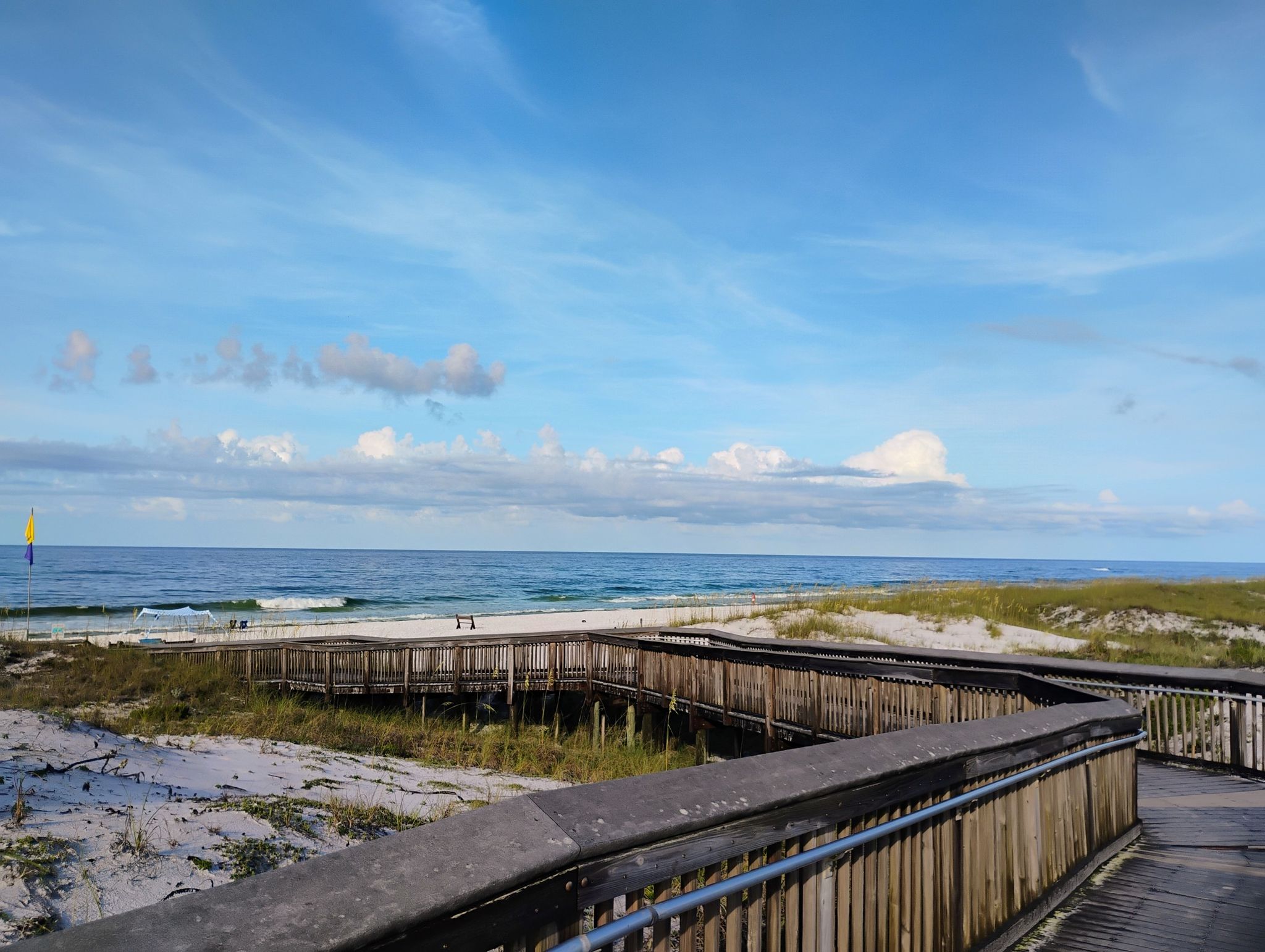 Wooden boardwalk curves towards a sunny beach and blue ocean under a cloudy sky. - Topsail Hill Reserve Beach loop
