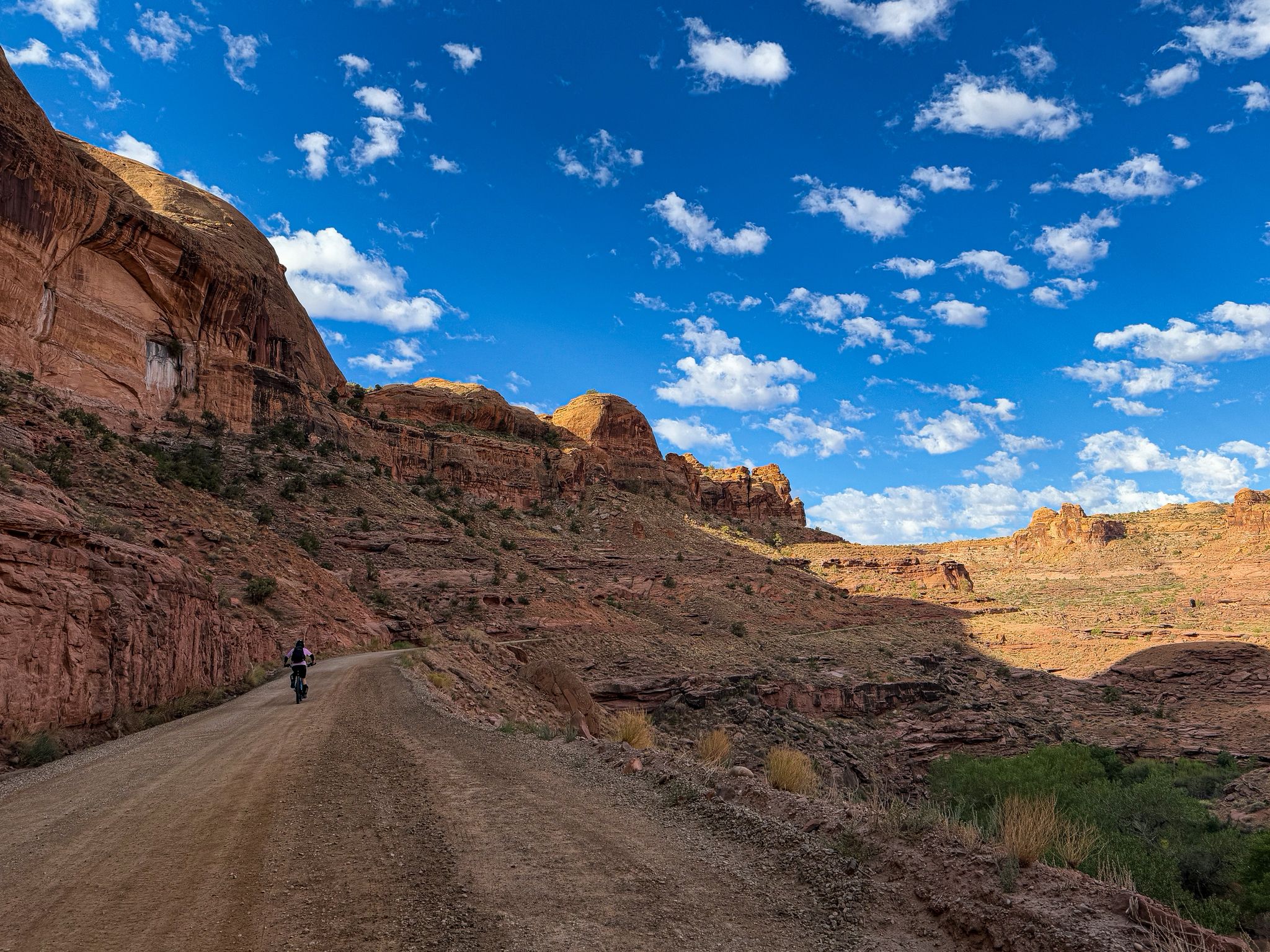 Cyclist on a dirt road through a red rock canyon, bright blue sky. - Hurrah Pass