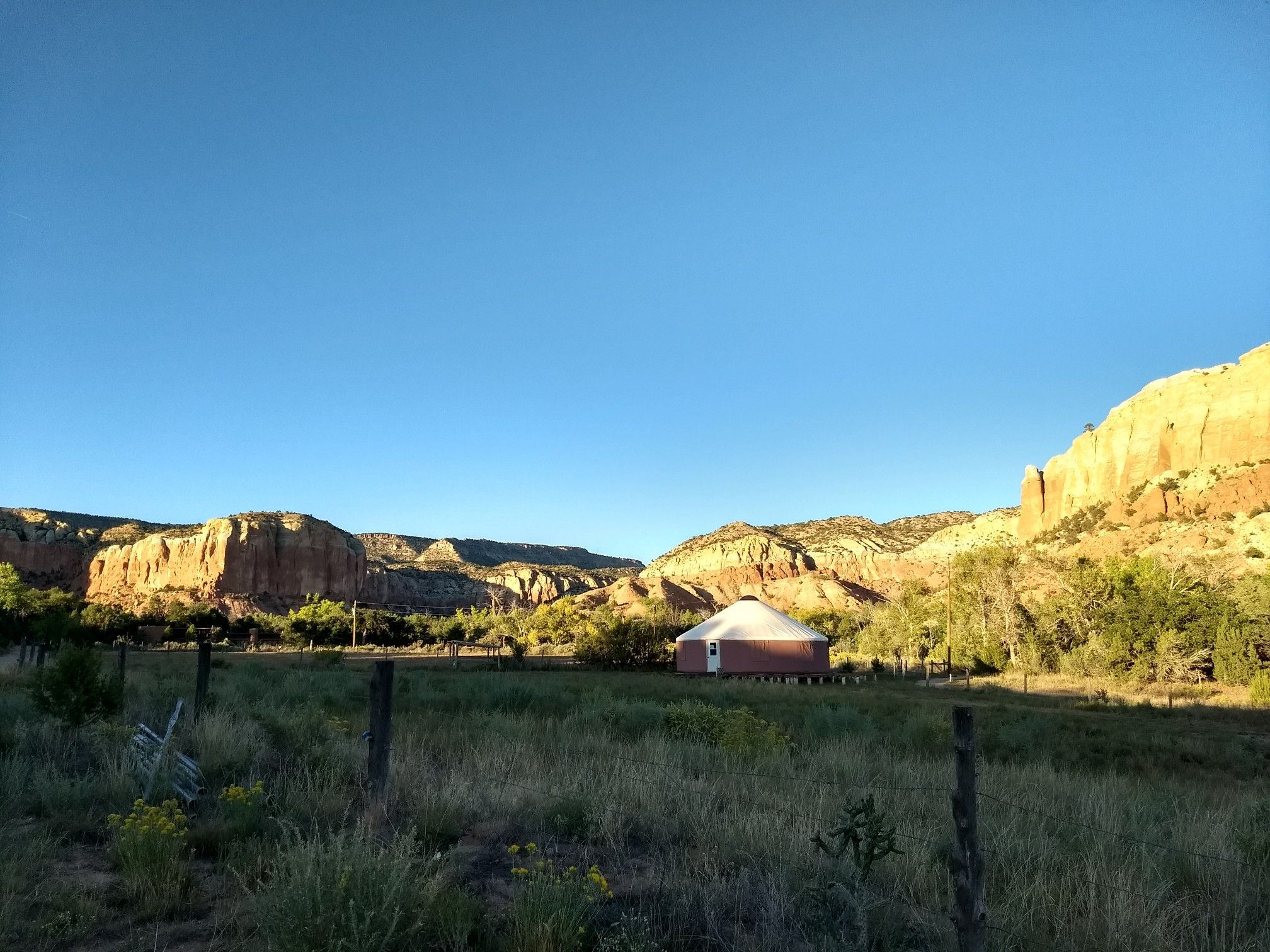 A yurt in a grassy field with large rock formations under a clear sky. - Kitchen Mesa Trail