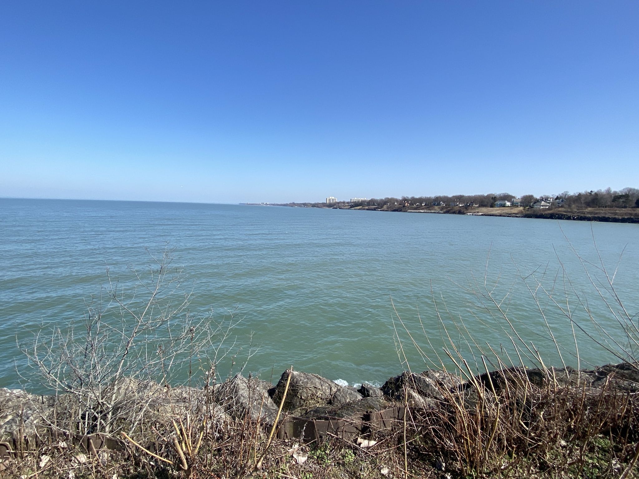 Calm blue water under clear sky, with rocky shore and distant land. - Perimeter Loop Trail