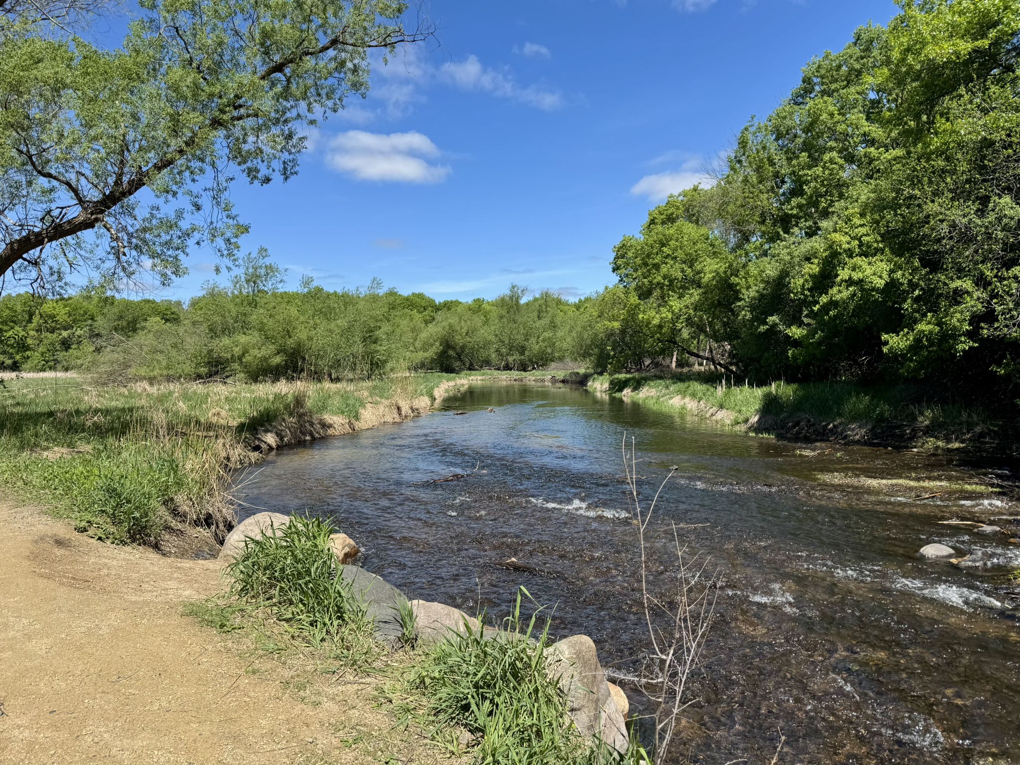 A winding river flows through a lush green landscape under a bright blue sky. - Minnetonka Loop Trail