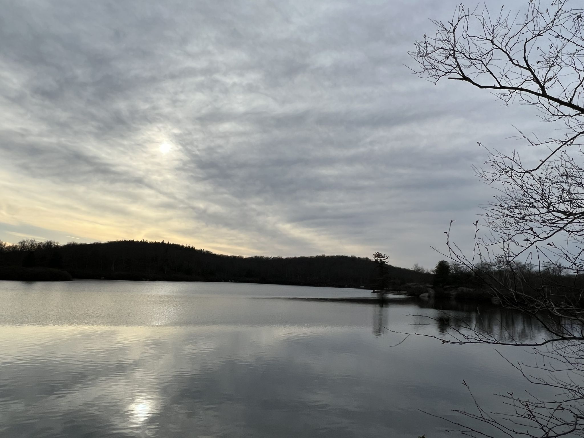 Calm lake reflects a dramatic, cloudy sky and dark, distant hills. - Pine Meadow Lake Loop