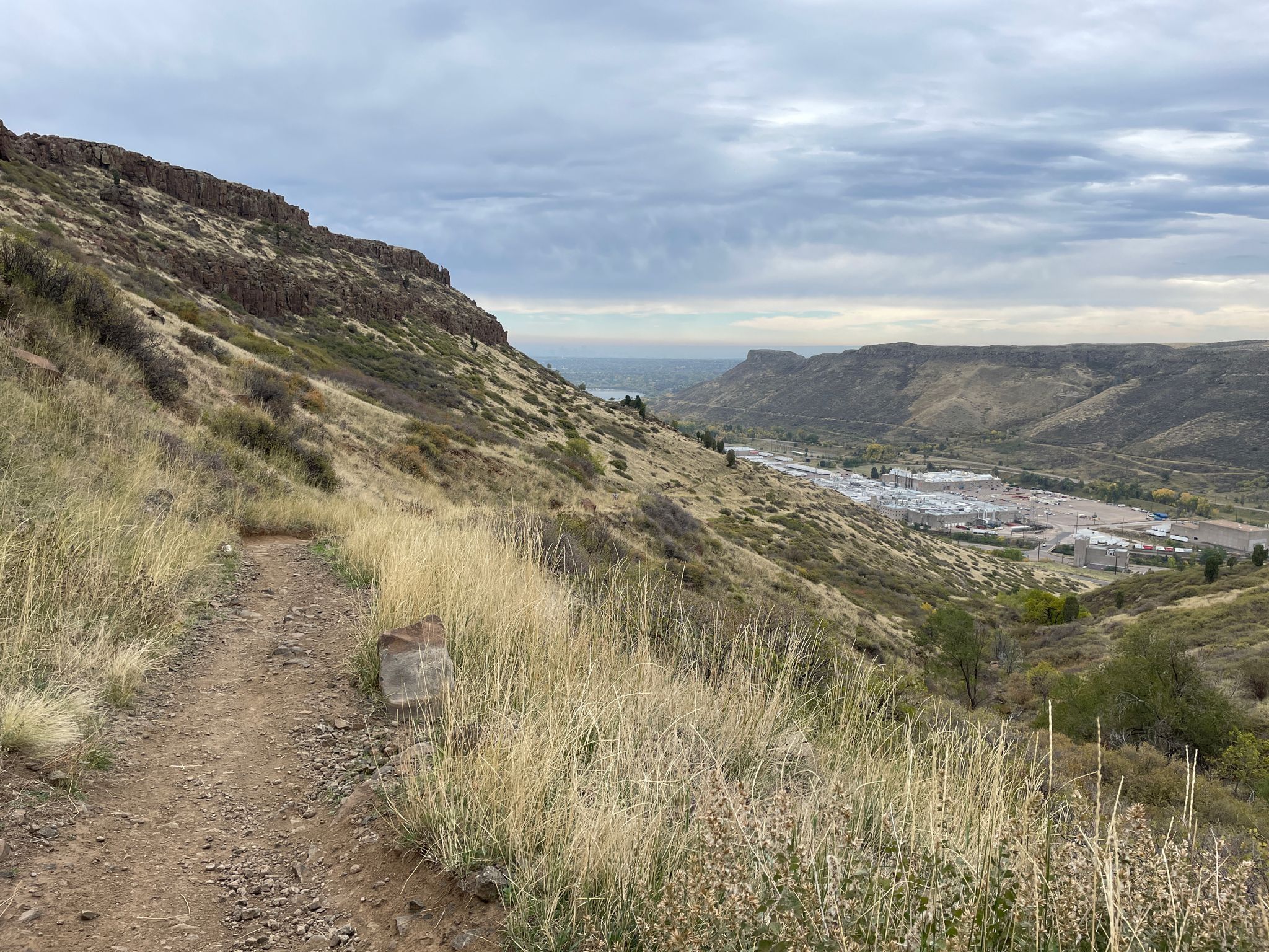 Dirt trail on a grassy hillside overlooking a valley with buildings. - North Table Loop Trail
