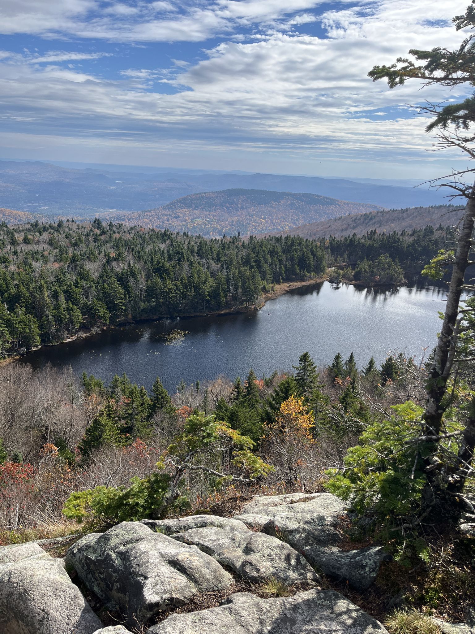 Overlook of a dark lake nestled in autumn forest with distant mountains. - Mount Sunapee via Newbury Trail