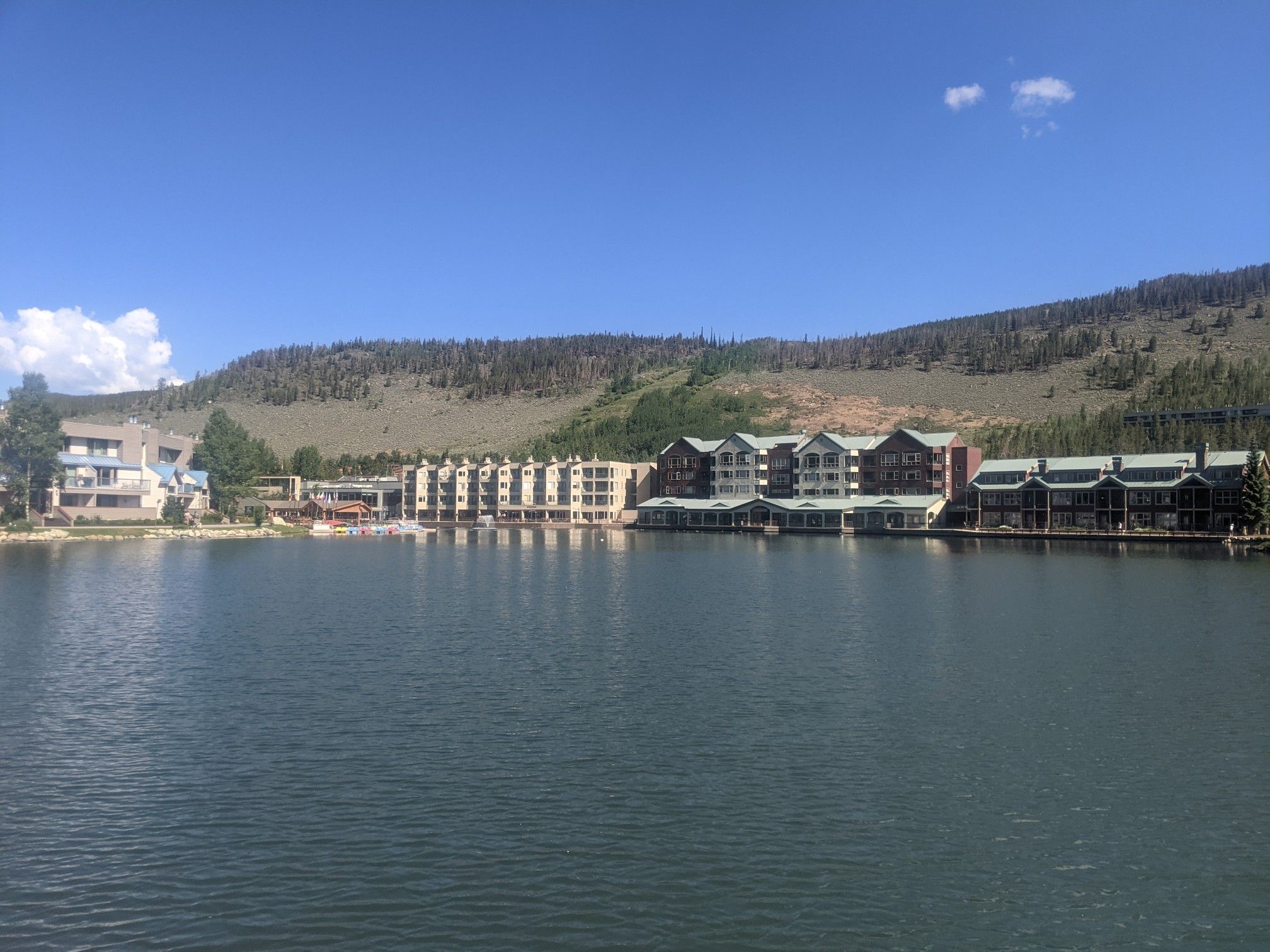 Lake with buildings and forested mountains under a bright, clear sky. - Keystone Lake loop from Keystone