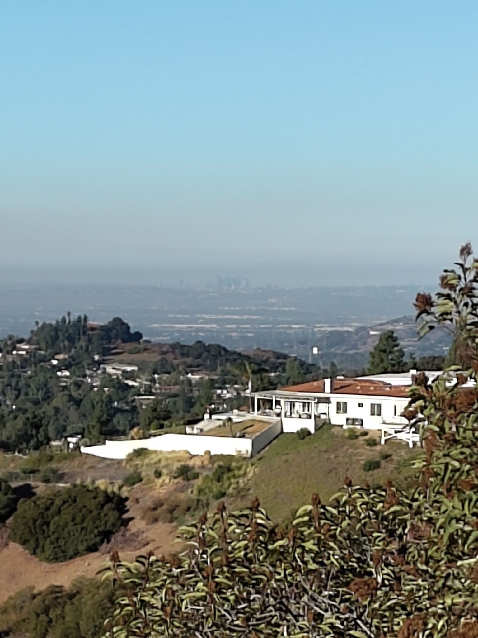 White house on a green hillside overlooking a hazy distant city. - Gale Mountain Loop