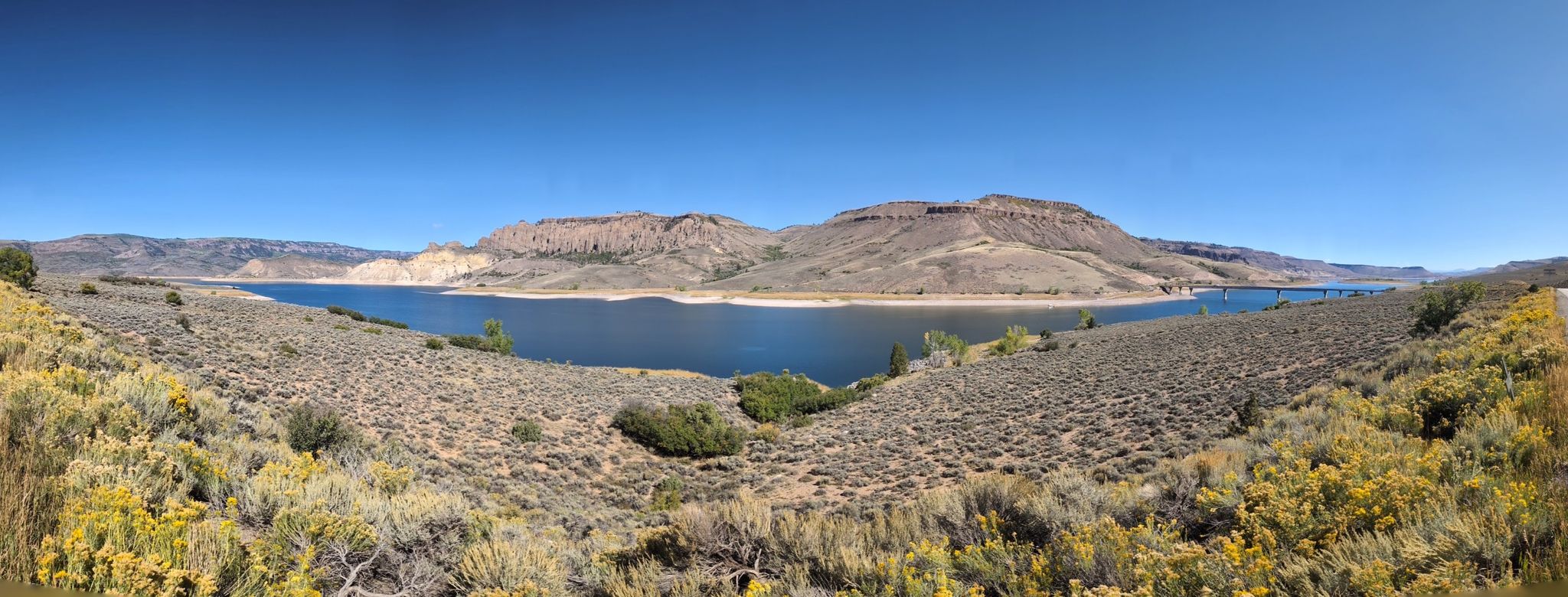 Panoramic view of a wide lake surrounded by arid hills and mountains. - Gunnison to Blue Mesa Dam Overlook