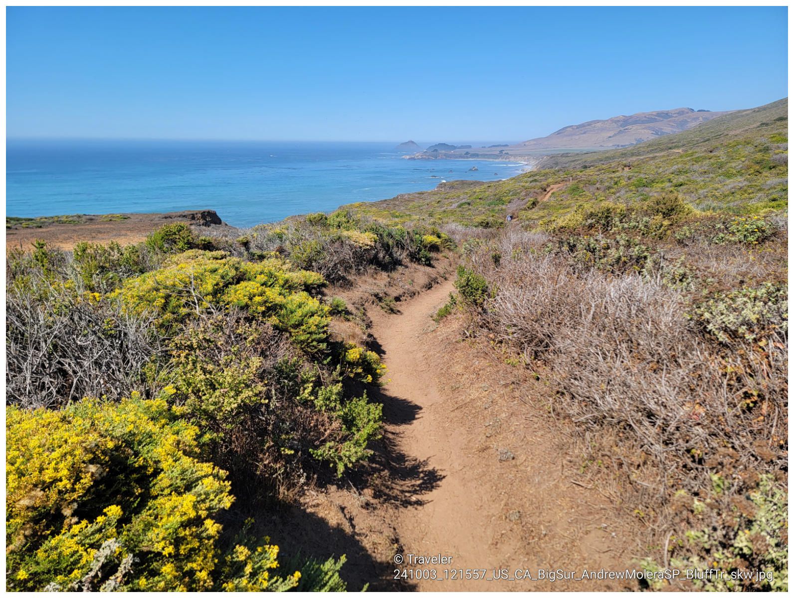 Sunny dirt path overlooking a vast blue ocean and distant green coastline. - Ridge, Panorama, and Bluffs Trail Loop