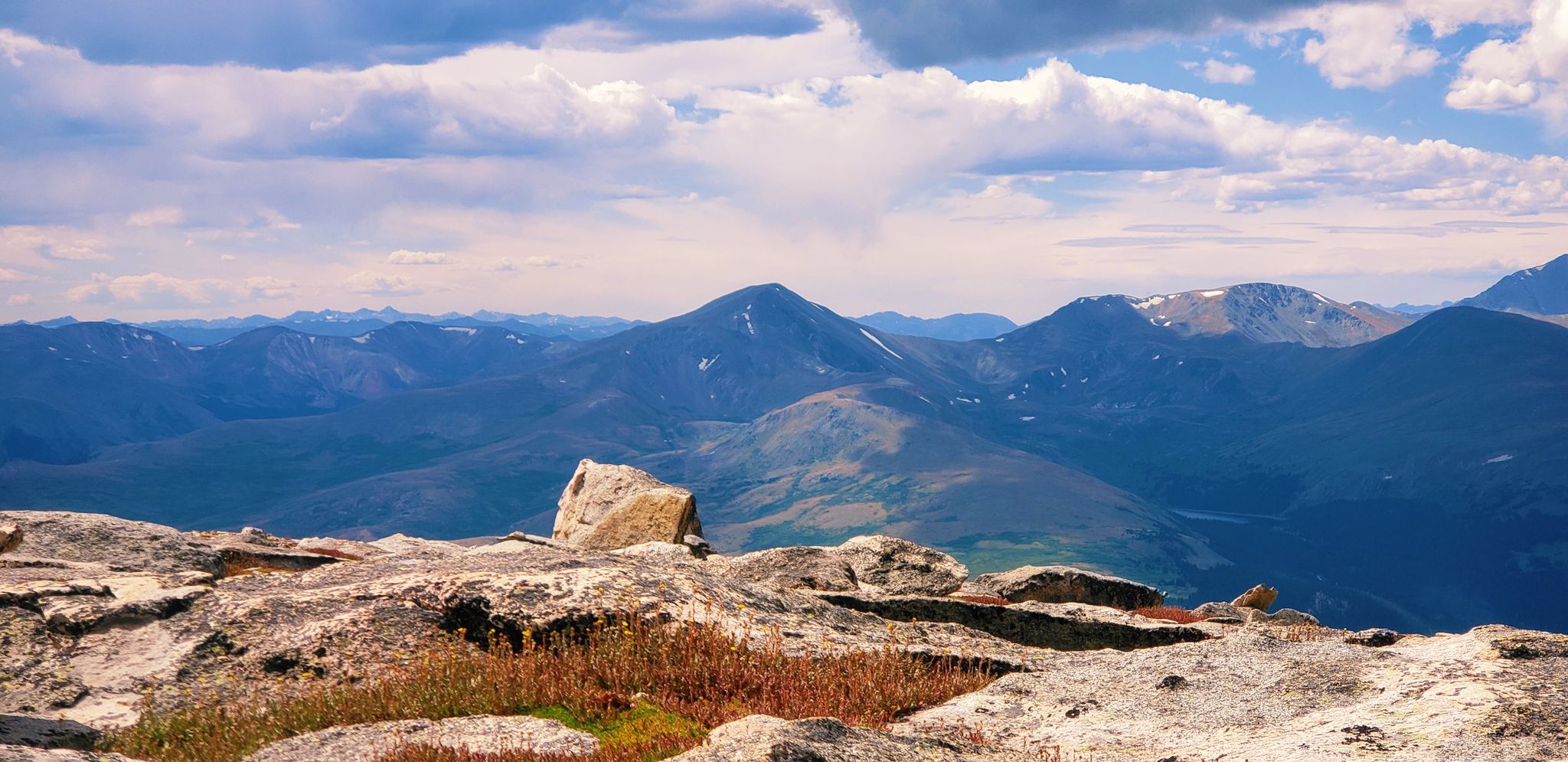 Rocky foreground overlooking a vast mountain range under a cloudy sky. - Mount Blue Sky Ridge Trail