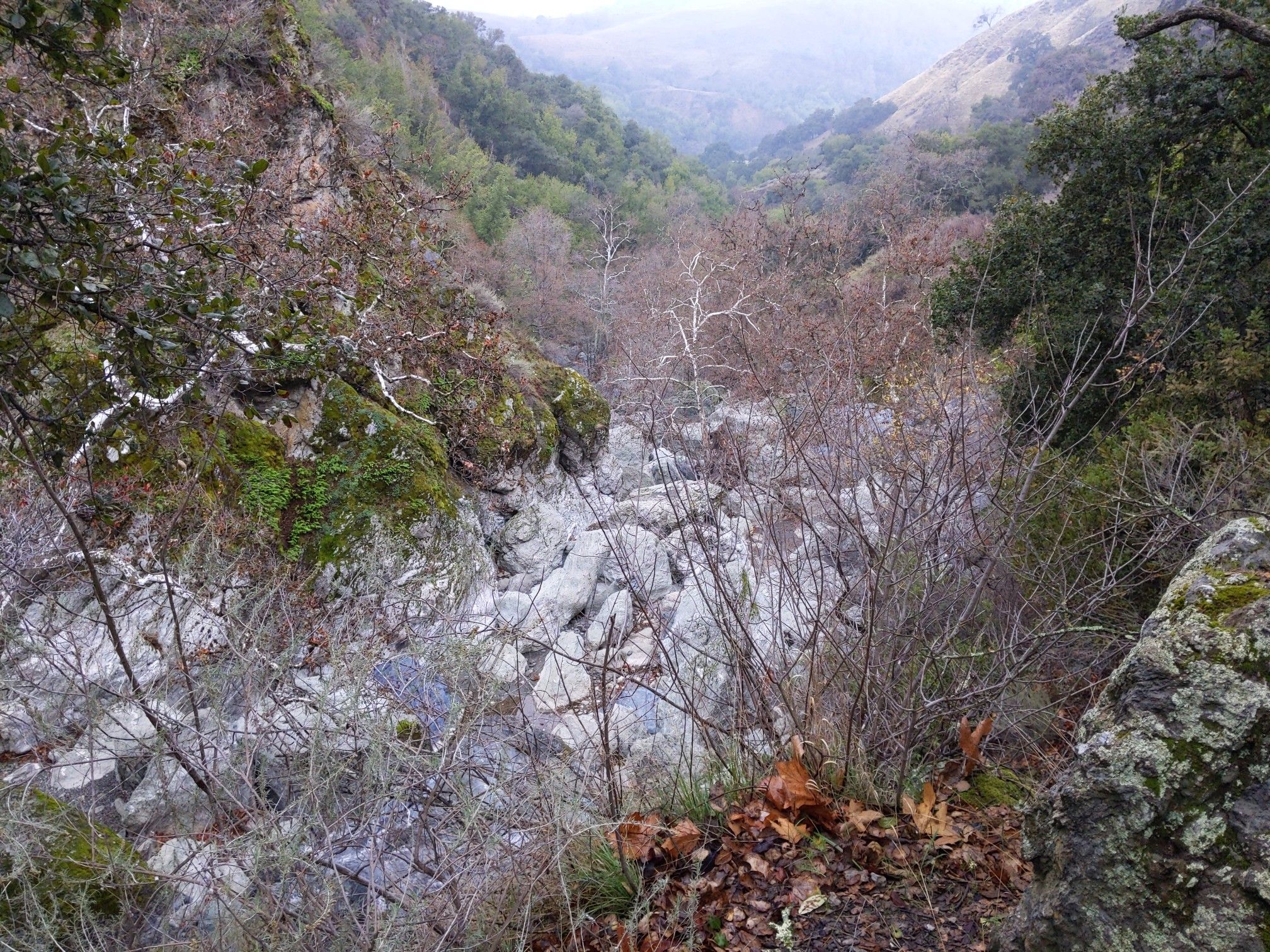 Rocky canyon with dry bushes and a distant valley under an overcast sky. - Little Yosemite loop from Sunol Regional Wilderness