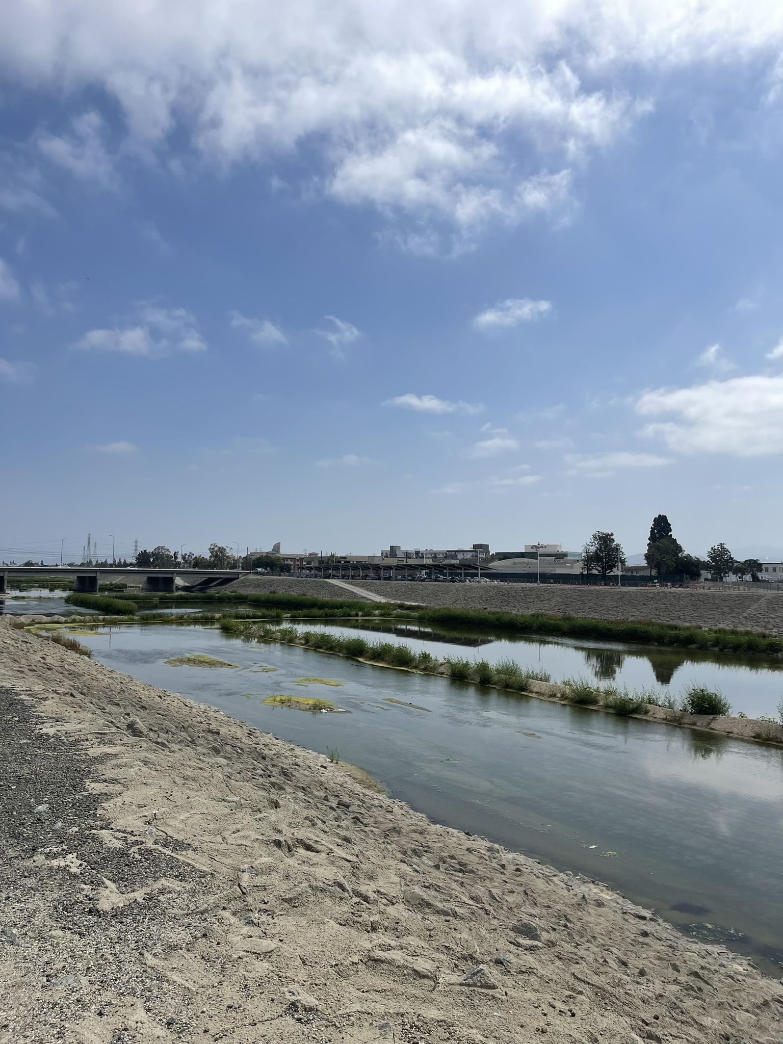 River flowing next to a sandy bank, with a bridge and buildings. - Angel Stadium loop from Disneyland