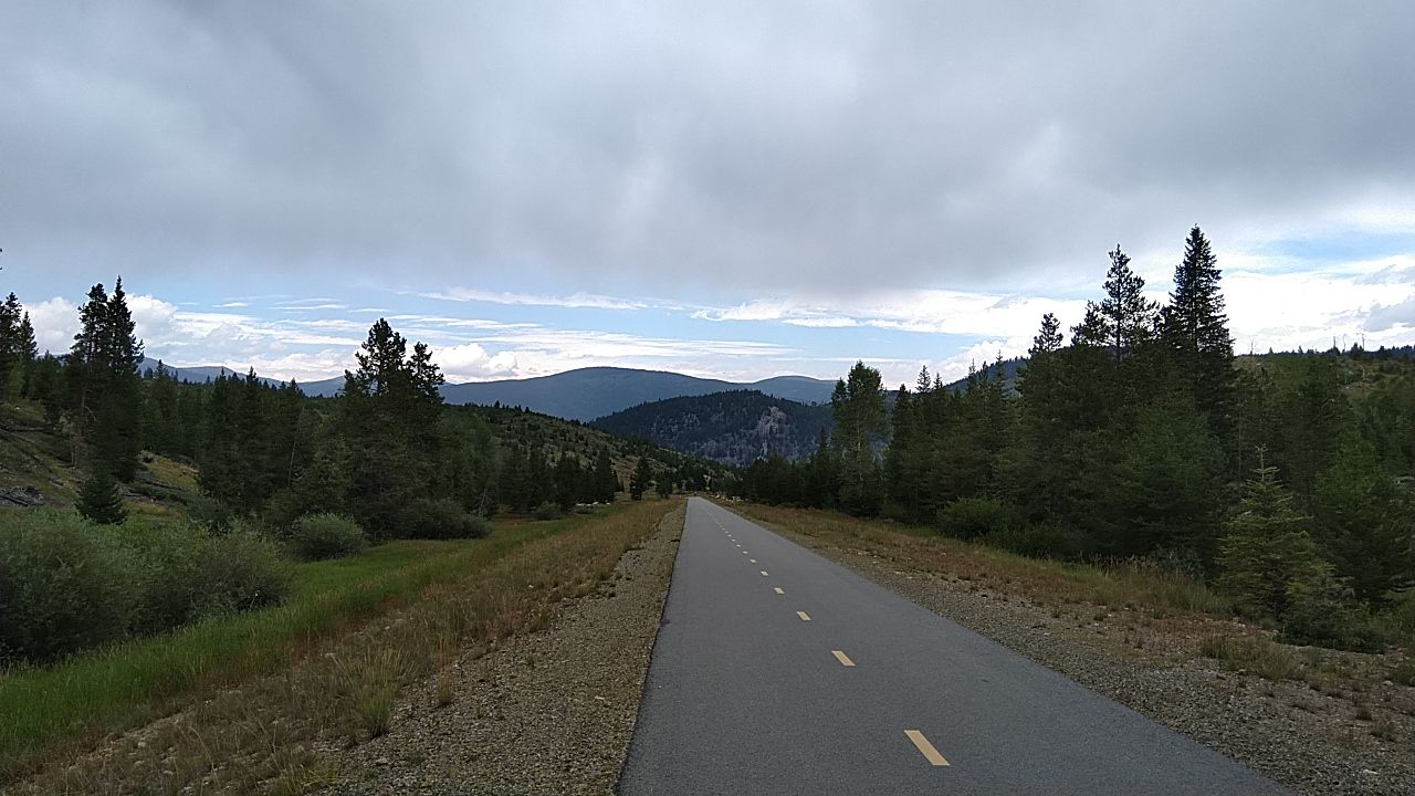 Paved path through a forested mountain landscape under an overcast sky. - Lakeshore Perimeter and Crown Point Road Loop