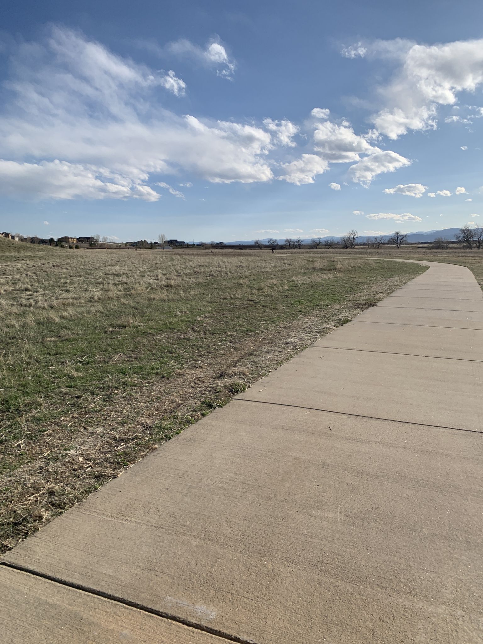 A winding paved path through a grassy field under a partly cloudy sky. - Coal Creek Trail