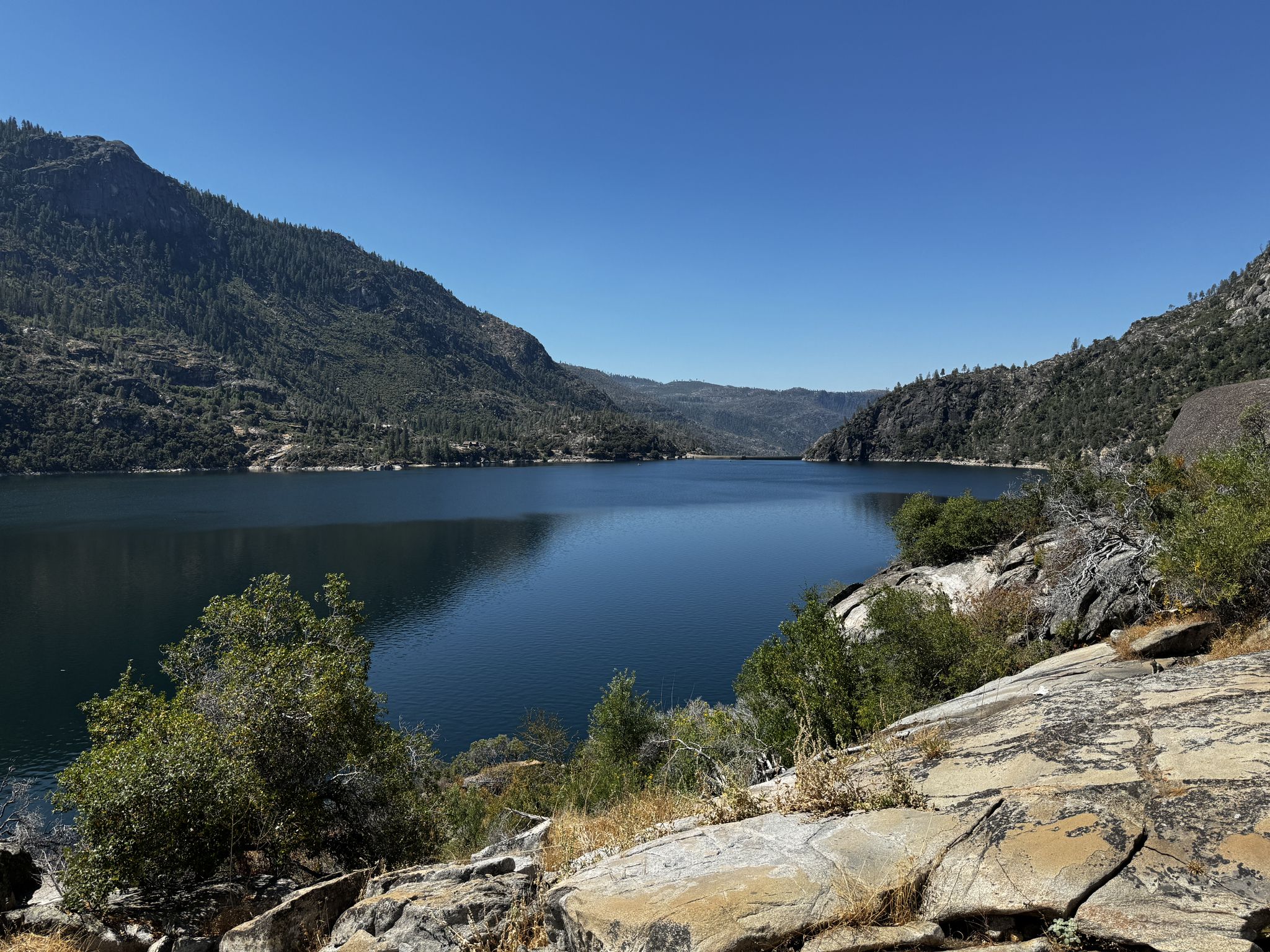 Wide lake surrounded by green, forested mountains under a clear blue sky. - Rancheria Falls Trail