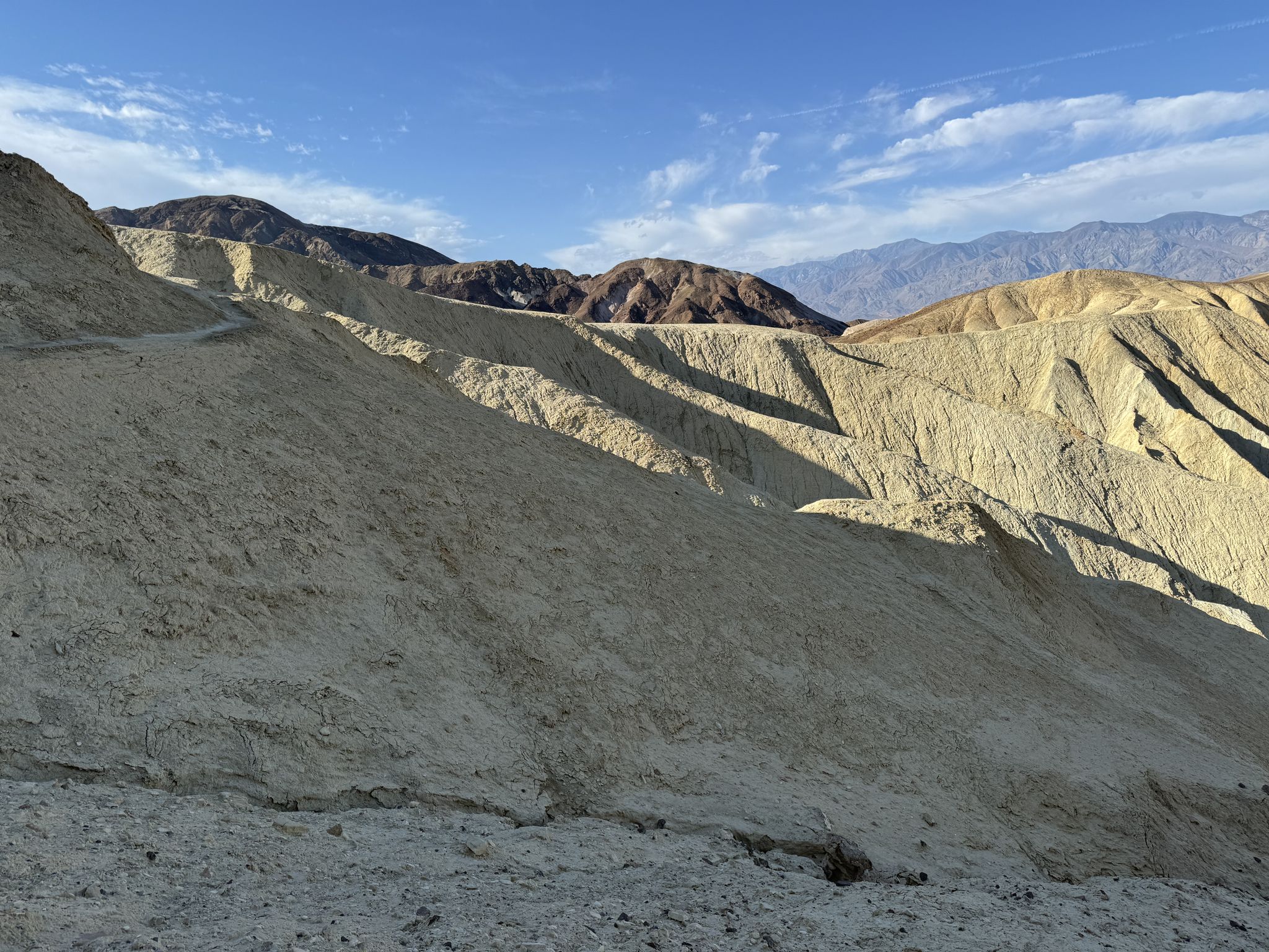 Sloping, light-colored desert hills with distant mountains under a blue sky. - Zabriskie Point – Manly Beacon loop from Zabriskie Point