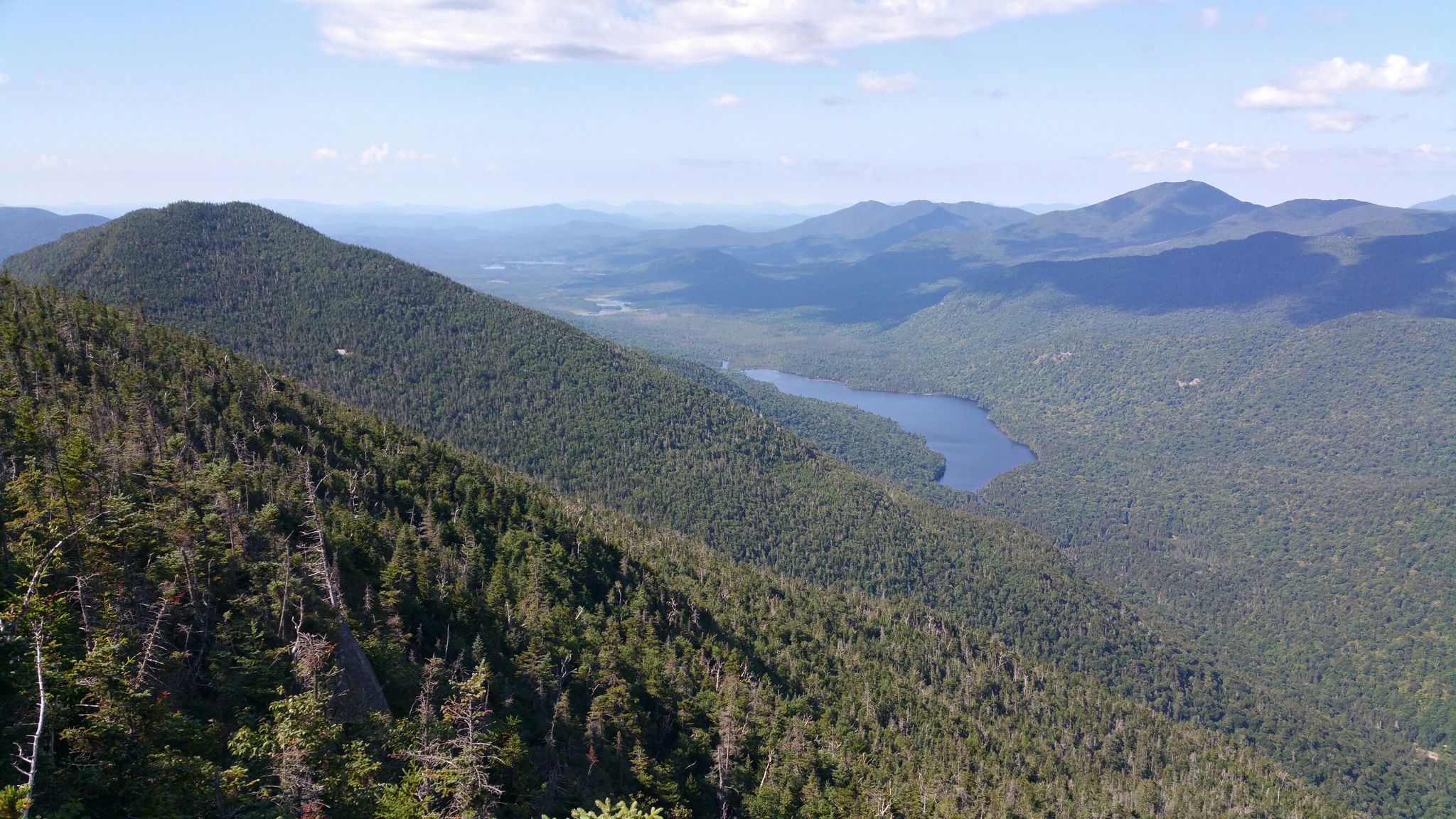 Panoramic view of vast forested mountains, a blue lake, under a bright sky. - Belfry Mountain loop from Pitchoff Mountain
