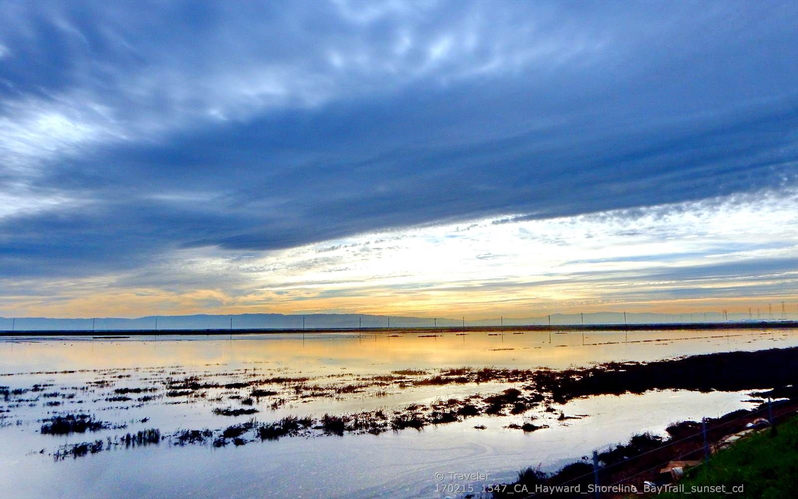 A dramatic sunset over a wide body of water with distant wind turbines. - SF Bay Trail through Eden Landing