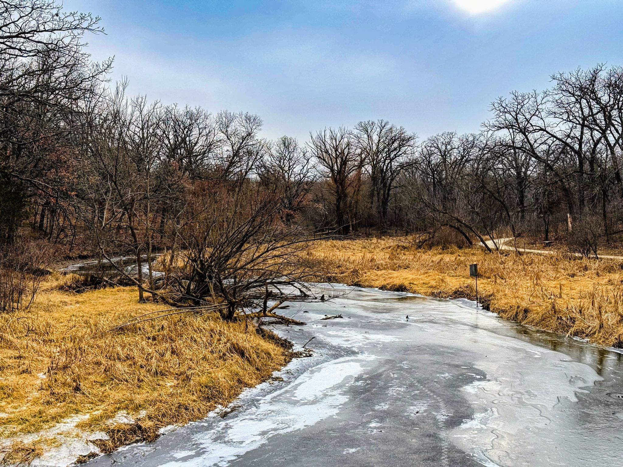 A partially frozen river winds through golden grass and bare trees on a sunny day. - Minnetonka Loop Trail