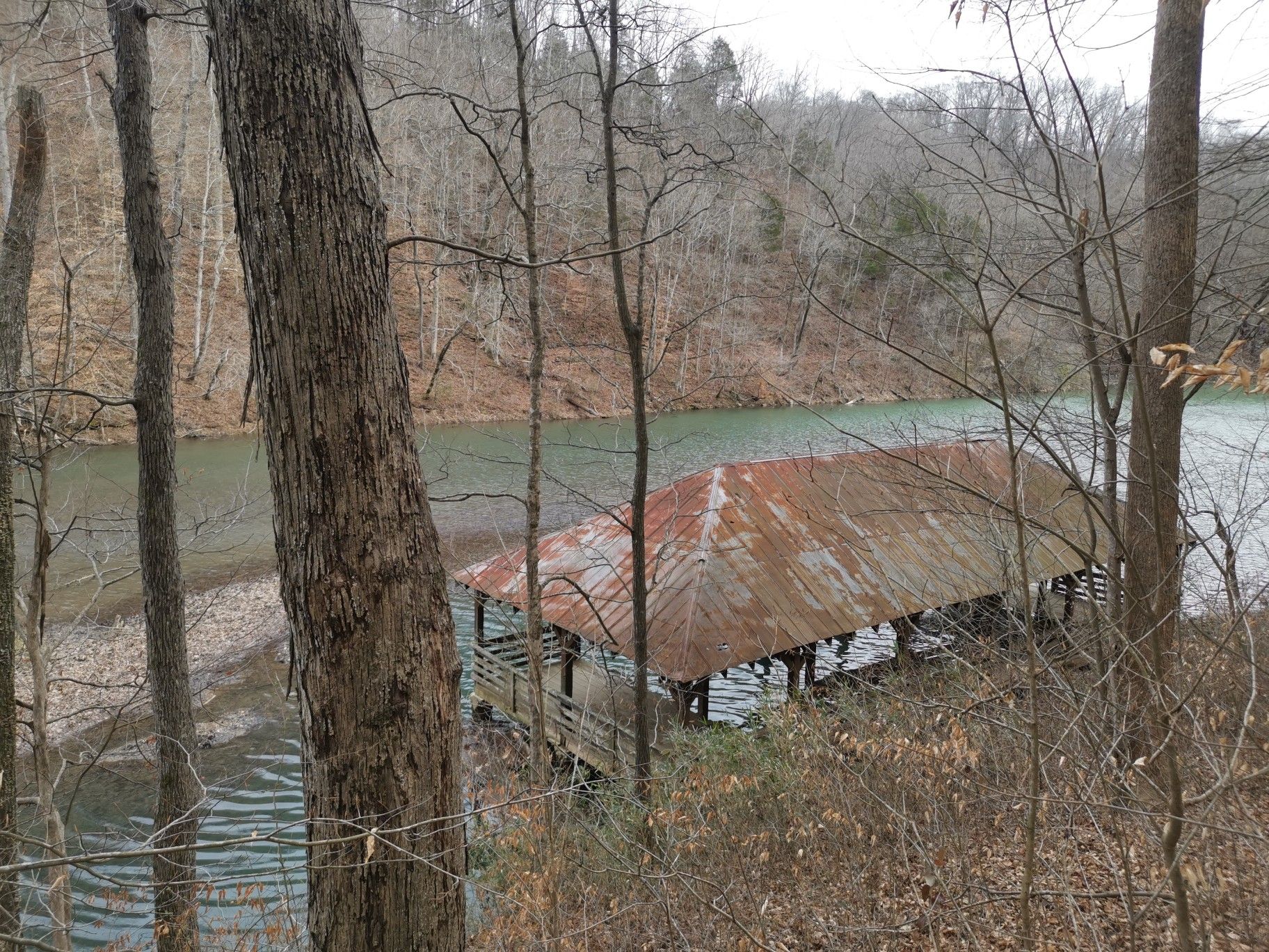 Rusty boat dock on a lake, seen through bare trees on an overcast day. - Standing Stone Lake Trail