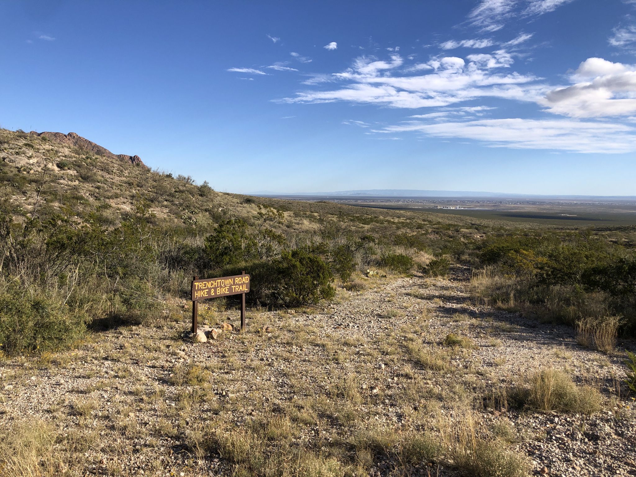 Desert landscape with a trail sign, distant mountains, and a clear blue sky. - Trans-Franklin Mountain Trail