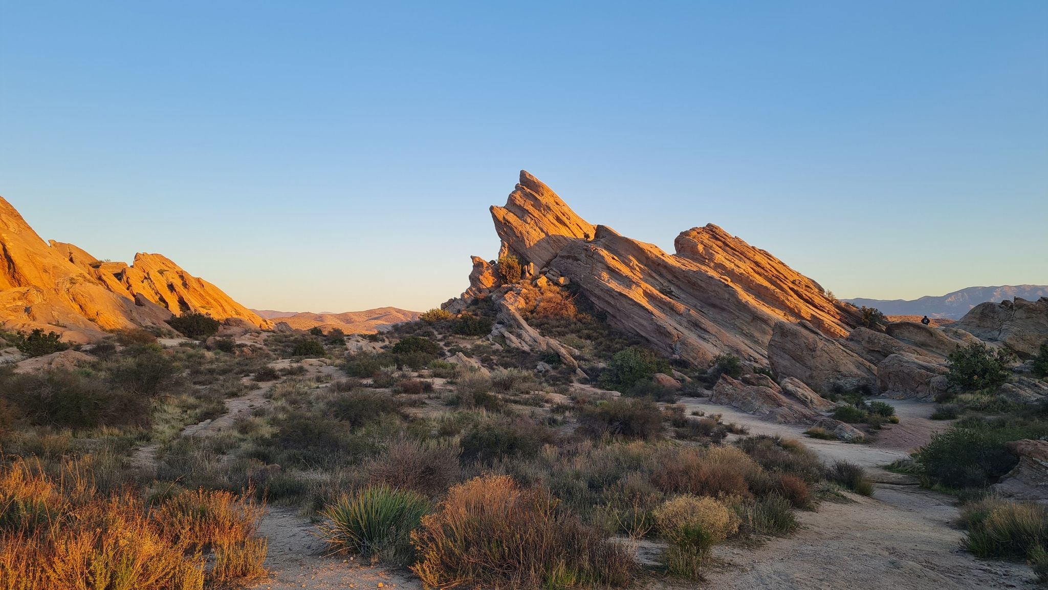 Jagged rock formations illuminated by golden hour light in a desert landscape. - Vasquez Rocks Loop