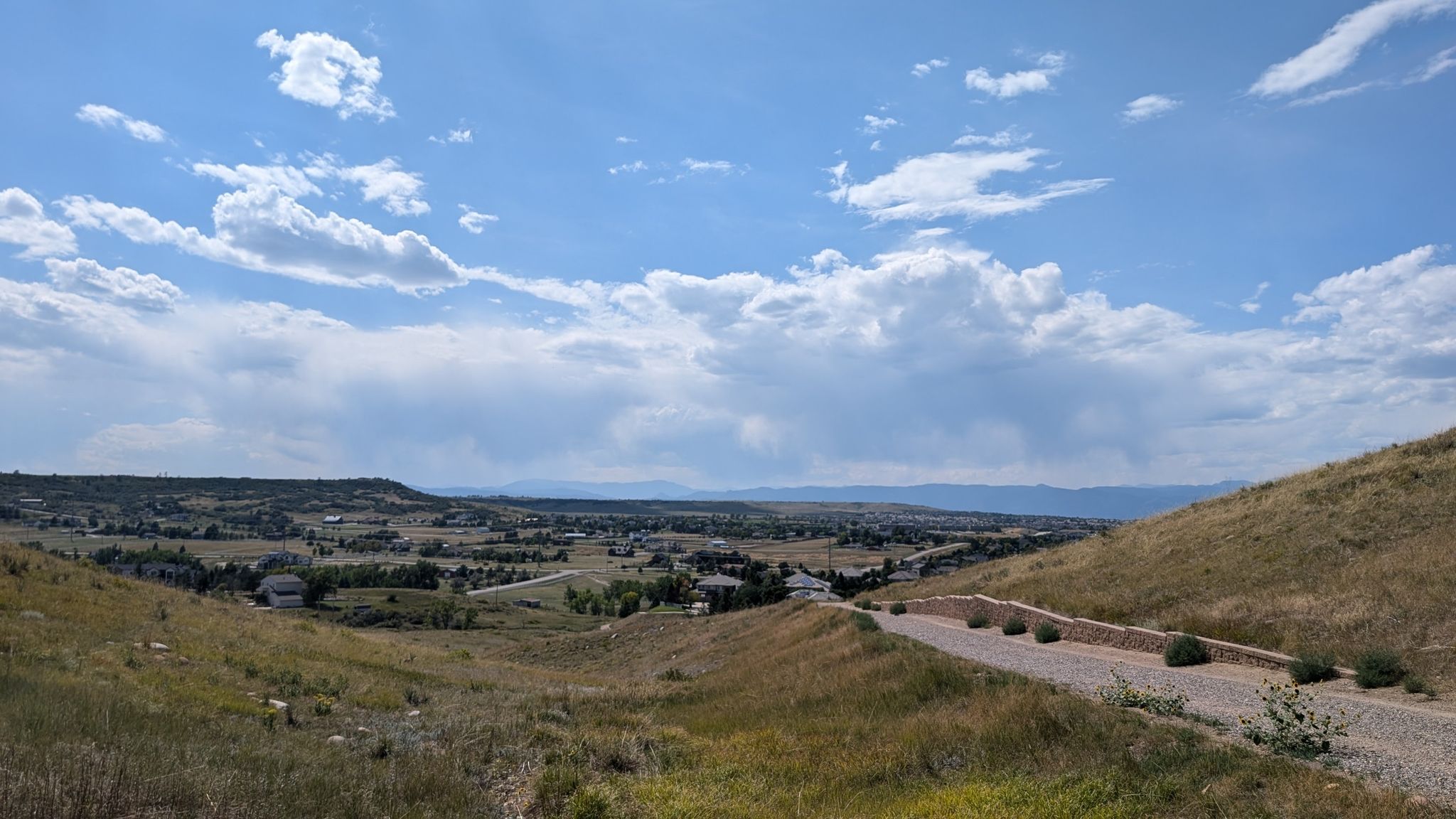 Expansive view of dry grassy hills, a path, distant town, and cloudy sky. - Highlands Point Viewpoint – Bluffs Regional Park loop from Sky Ridge