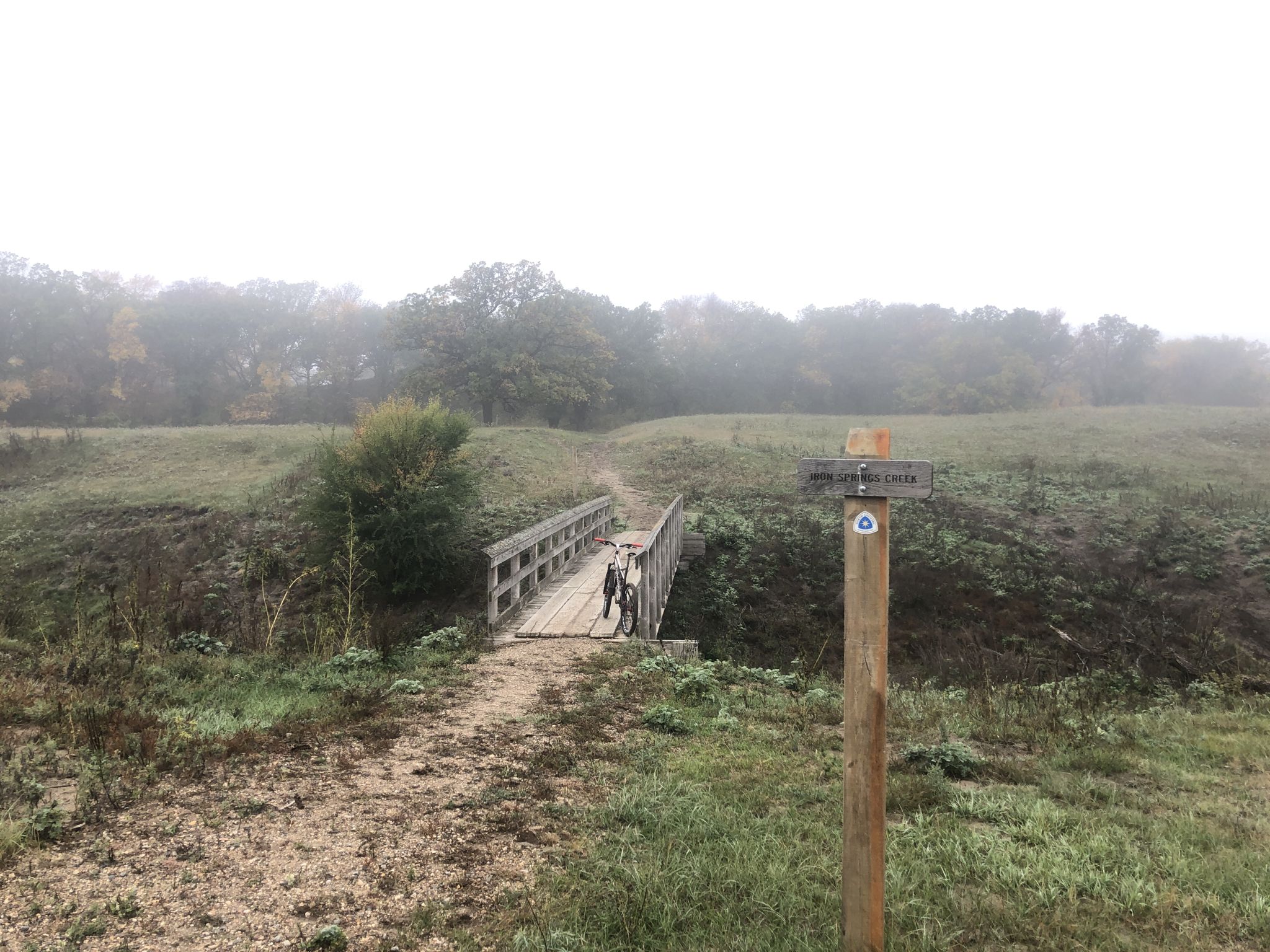 Two people walk across a wooden bridge in a foggy, grassy landscape. - North Country National Scenic Trail