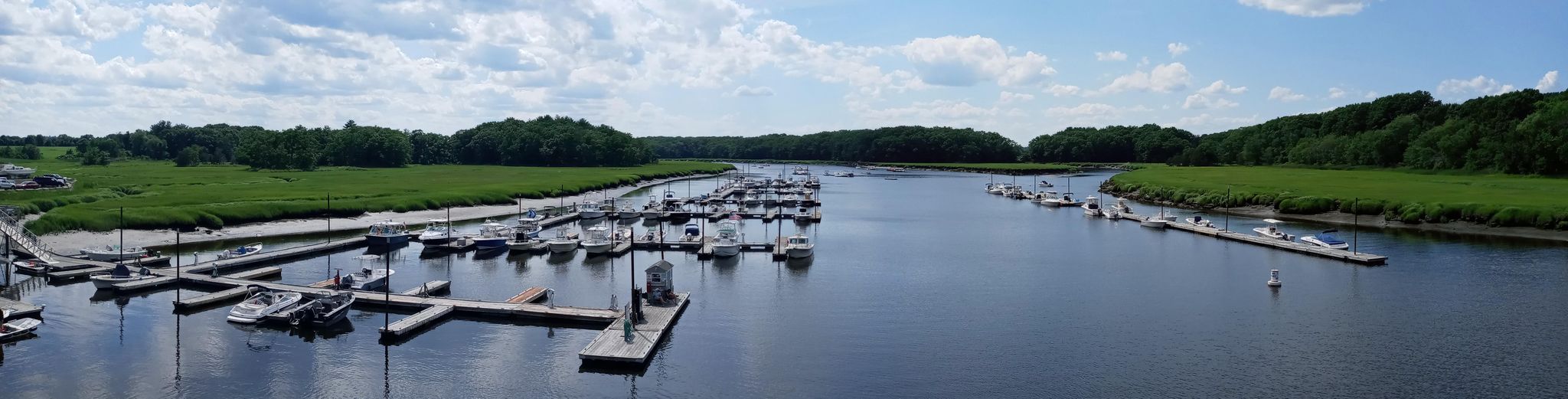 Panoramic river view with boats docked at marinas, green marshlands, and cloudy sky. - Parker River Bridge – Clipper City Rail Trail loop from Newburyport