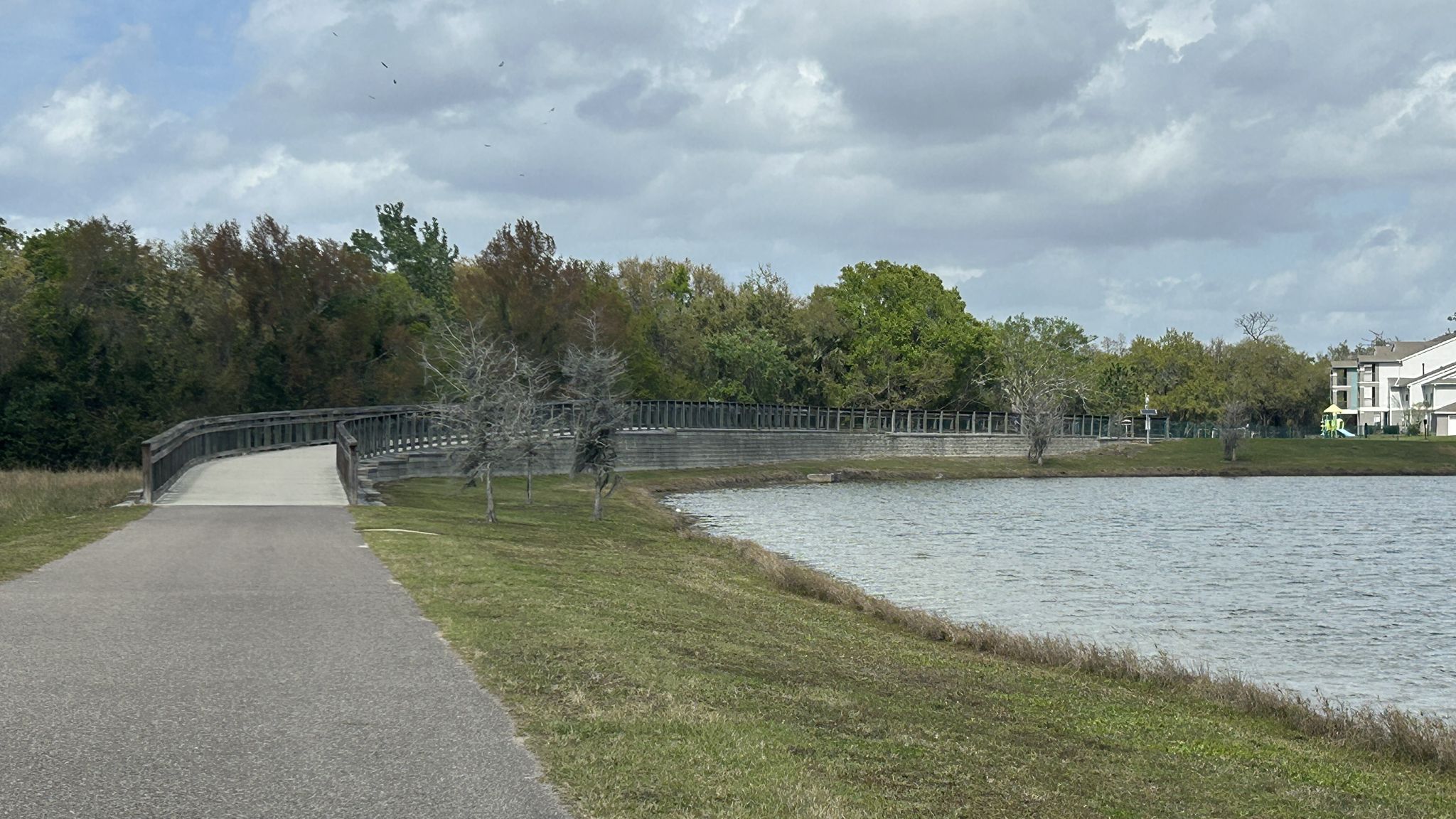 Paved path leads to a long bridge over a lake under cloudy skies. - Shingle Creek Regional Trail