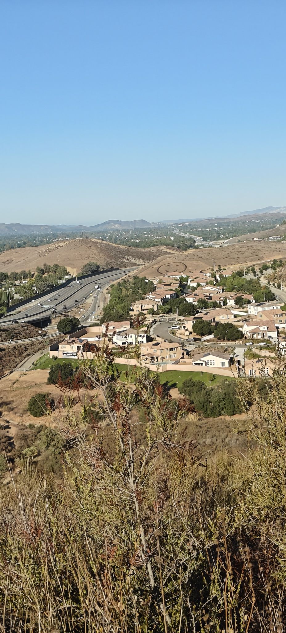 Bright daylight view of a valley with houses, a highway, and dry hills. - Hummingbird Trail Loop