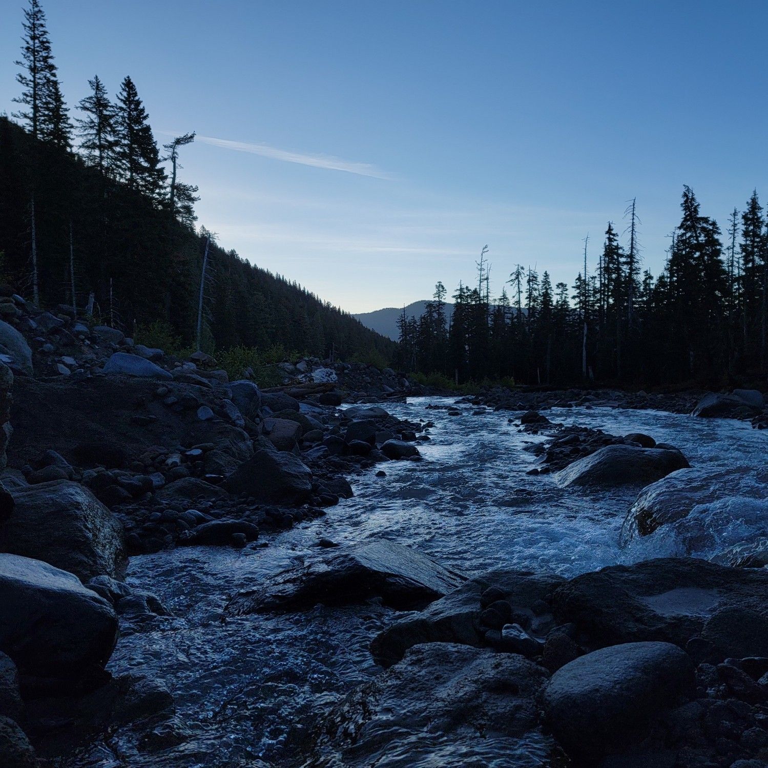 Rushing river flowing through a dark, rocky forest under a twilight sky. - Elk Meadows Trail #645