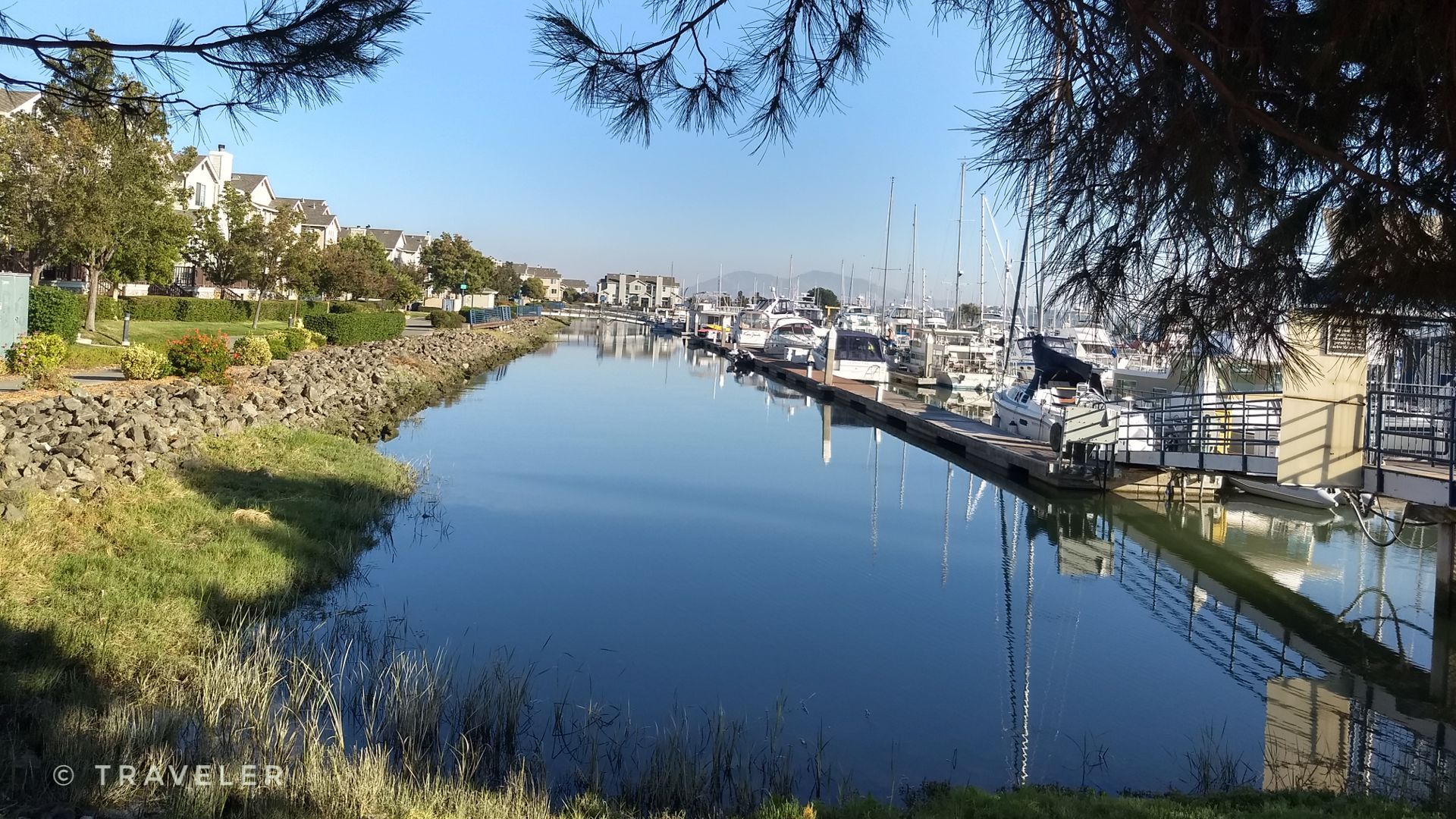 Calm waterway with docked boats, houses, and green banks on a sunny day. - San Francisco Bay Trail: Benicia Marina Loop