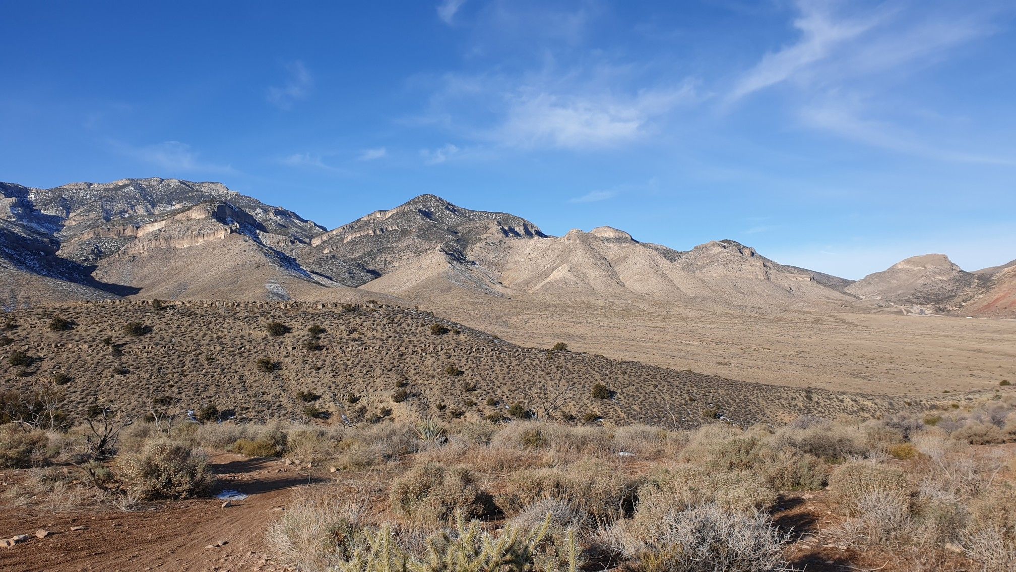 An expansive desert landscape with mountains, sparse vegetation, and a clear blue sky. - Badger Pass Loop