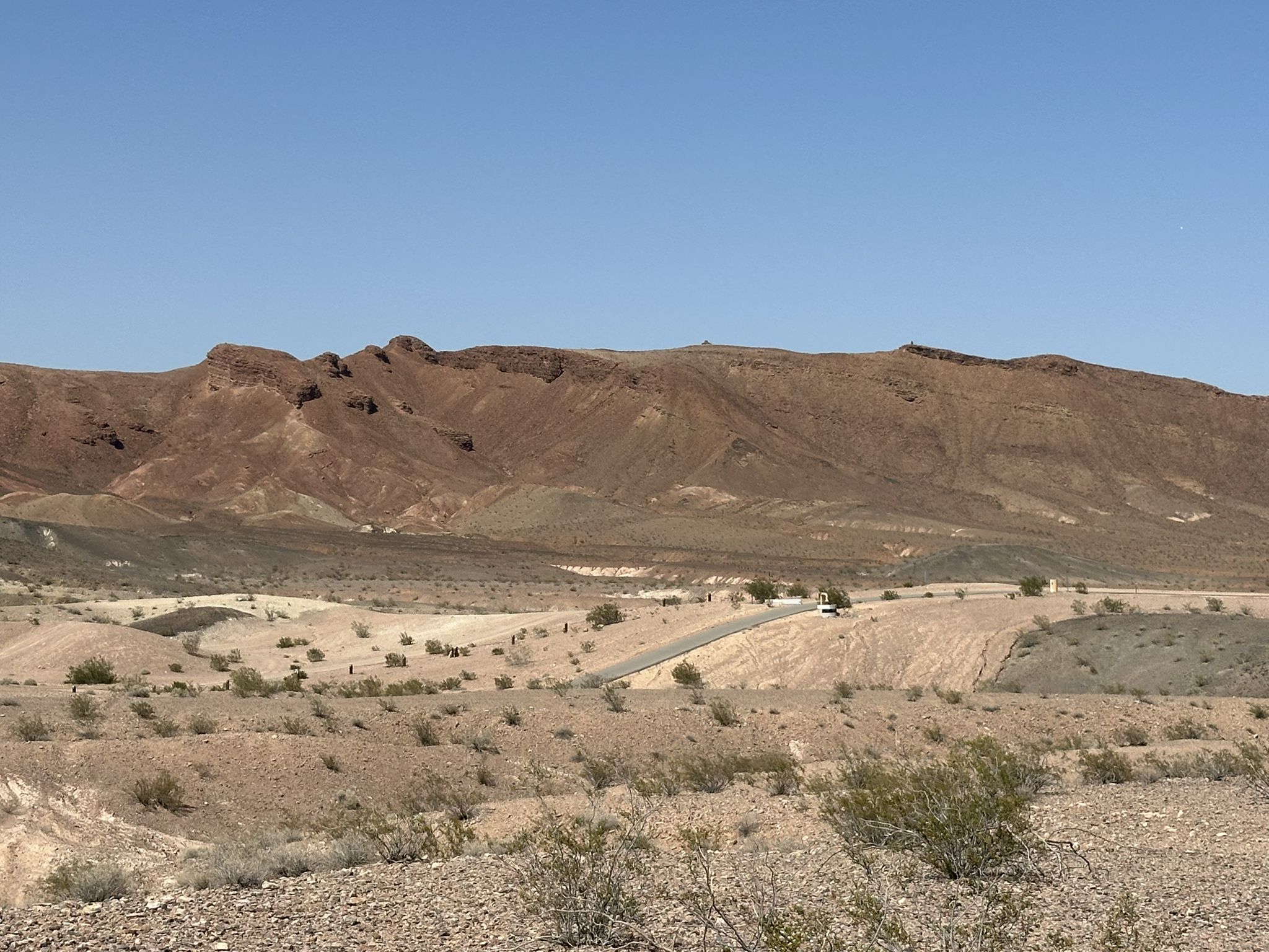 Wide desert landscape with a paved road leading to distant brown mountains. - Wetlands loop