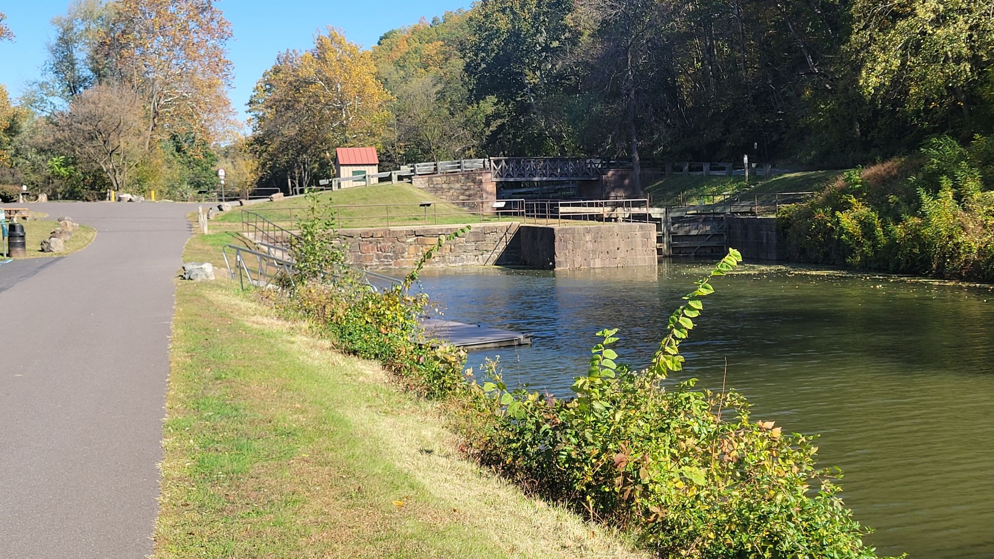 Canal lock with a small building, next to a paved path and autumn trees. - Lock 60 loop from Phoenixville