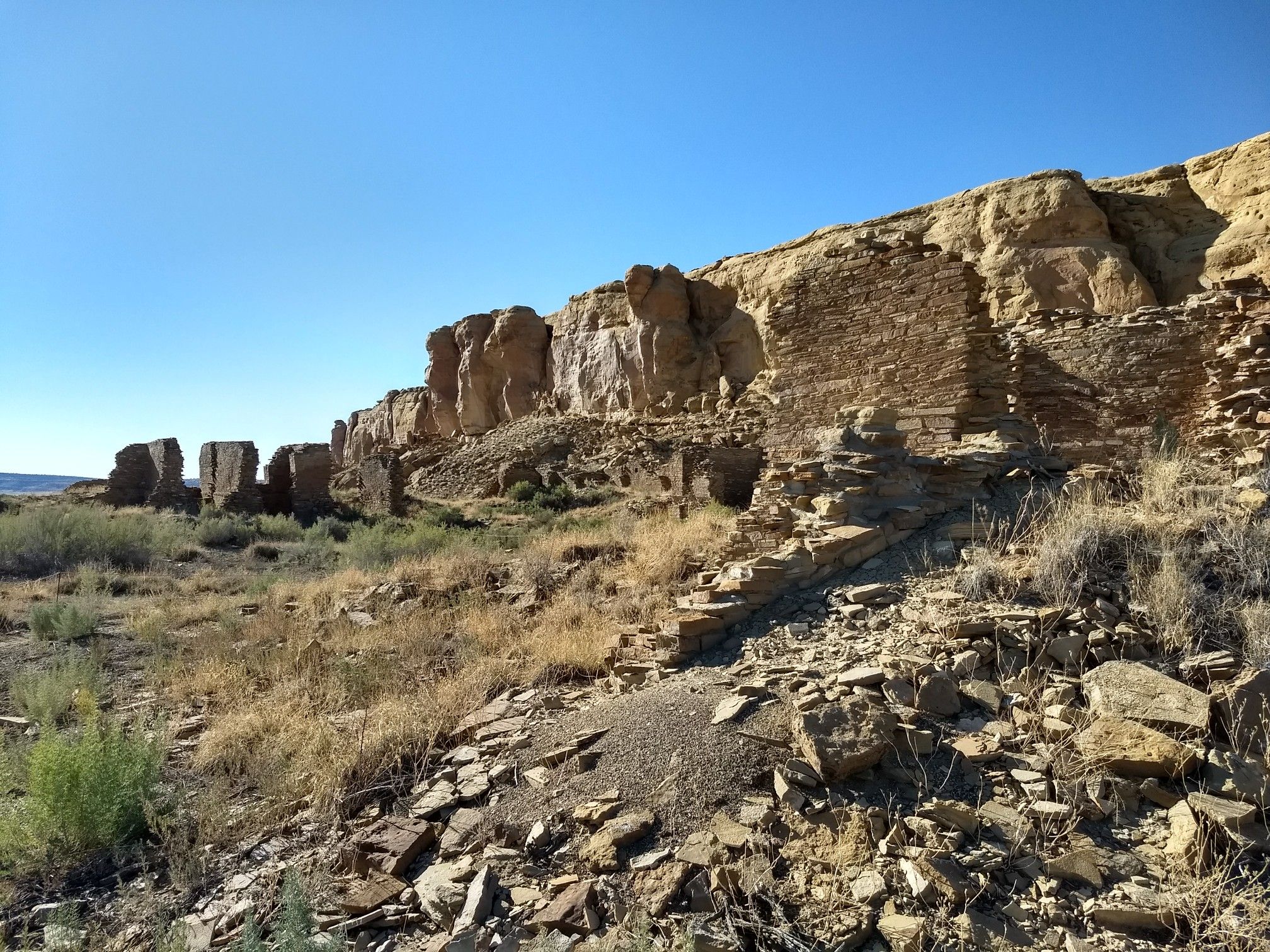 Ancient stone ruins at cliff base, dry landscape, clear sky. - Wijiji Trail